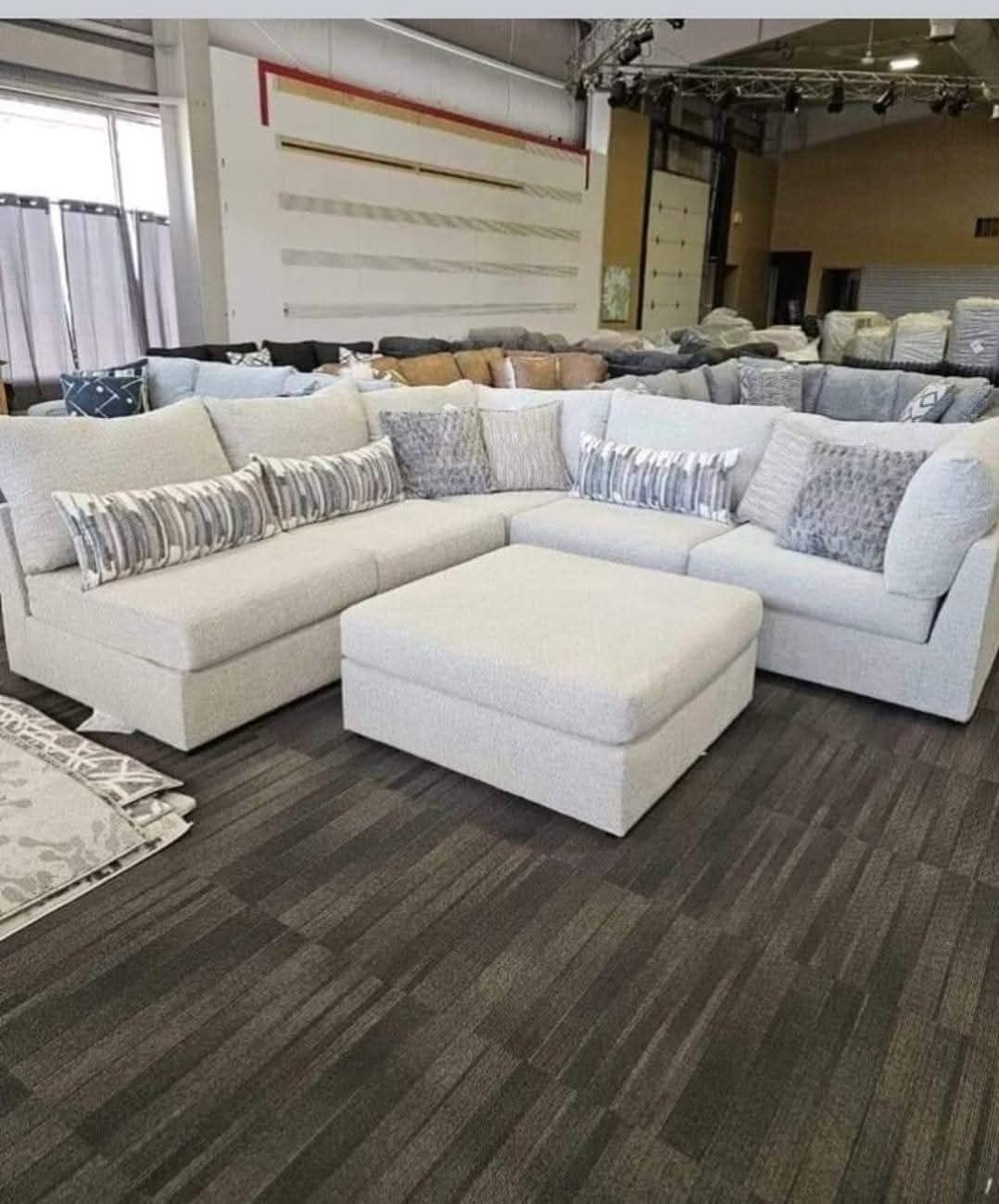 Gray sectional sofa in a showroom. Gray carpeted floor, shelves in background.