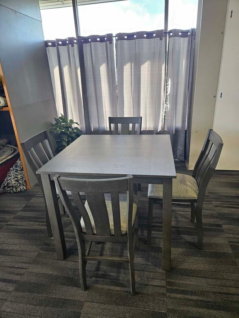 Gray dining table and four matching chairs in a room with a large window and gray curtains.