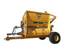 Yellow Vermeer SPX9010 hay baler, with a wheel and attached to a tractor.