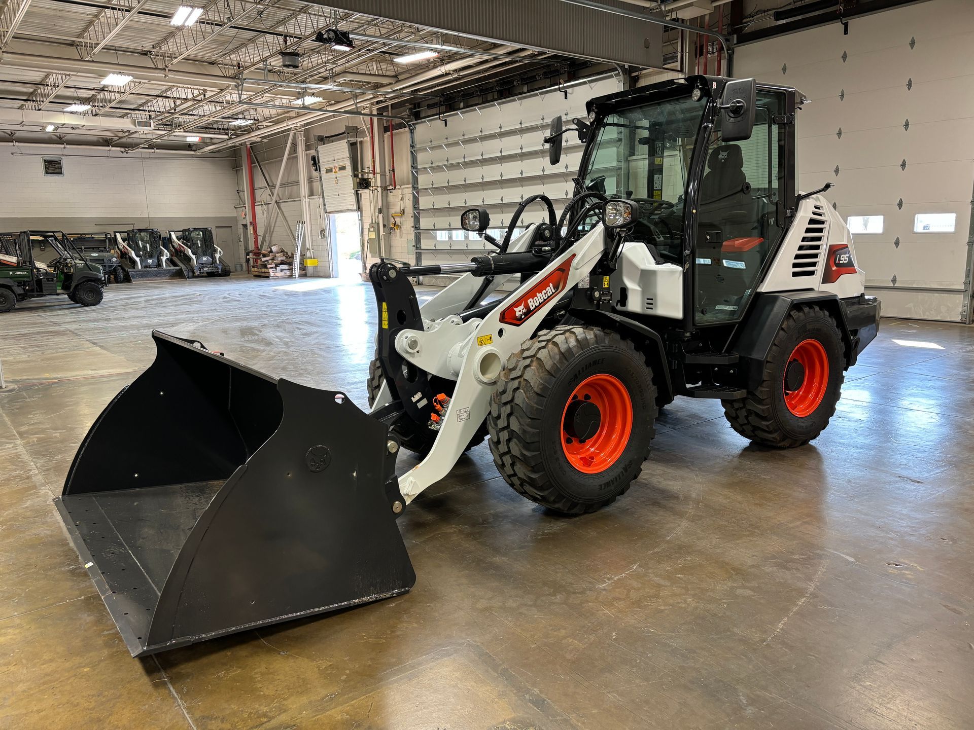 Bobcat compact loader with a black bucket, indoors on a concrete floor.