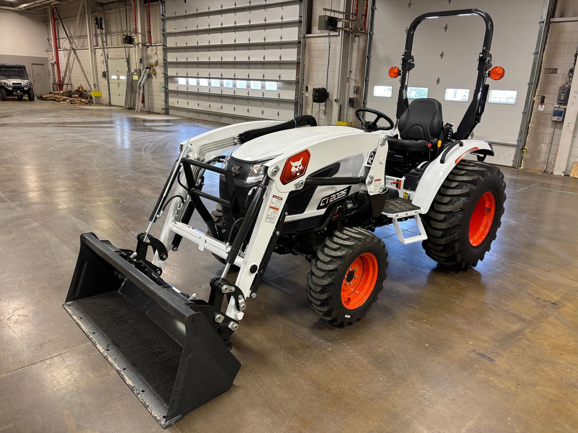 White and orange Bobcat tractor with a front-end loader inside a garage.
