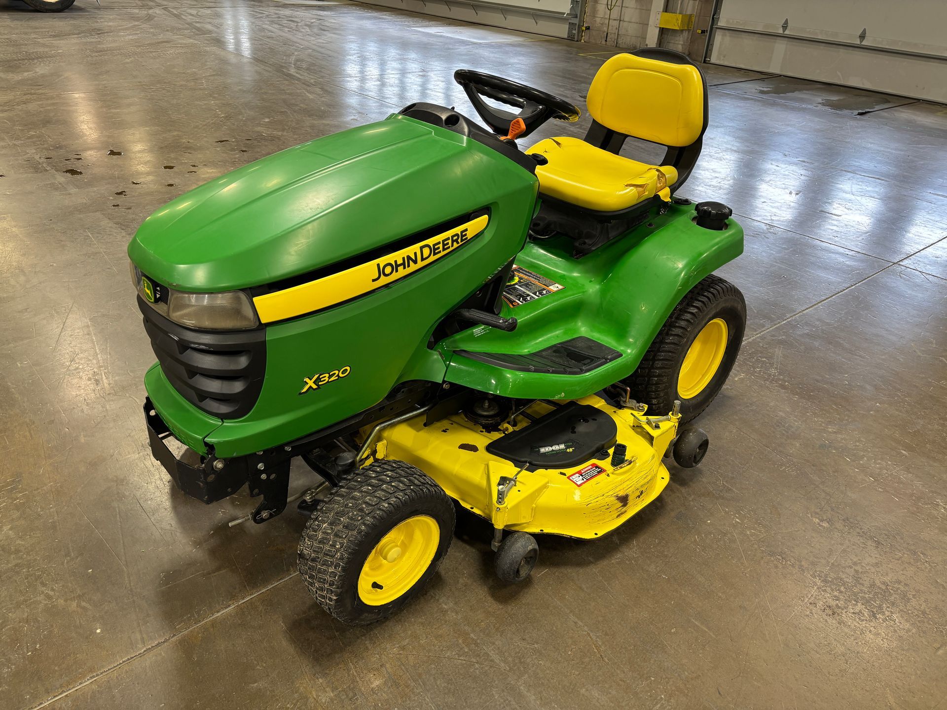 Green and yellow John Deere X300 riding lawnmower on a concrete floor.