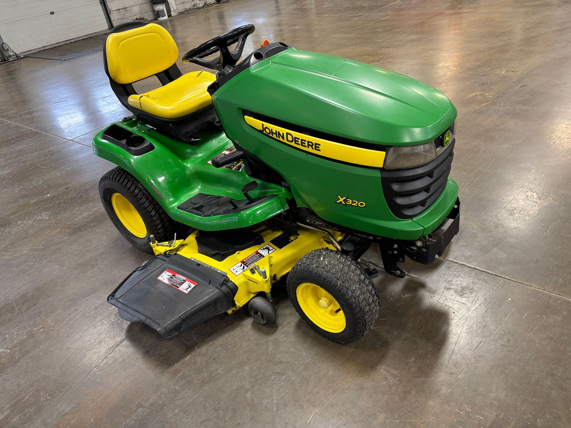 Green and yellow John Deere riding lawn mower on a concrete surface.