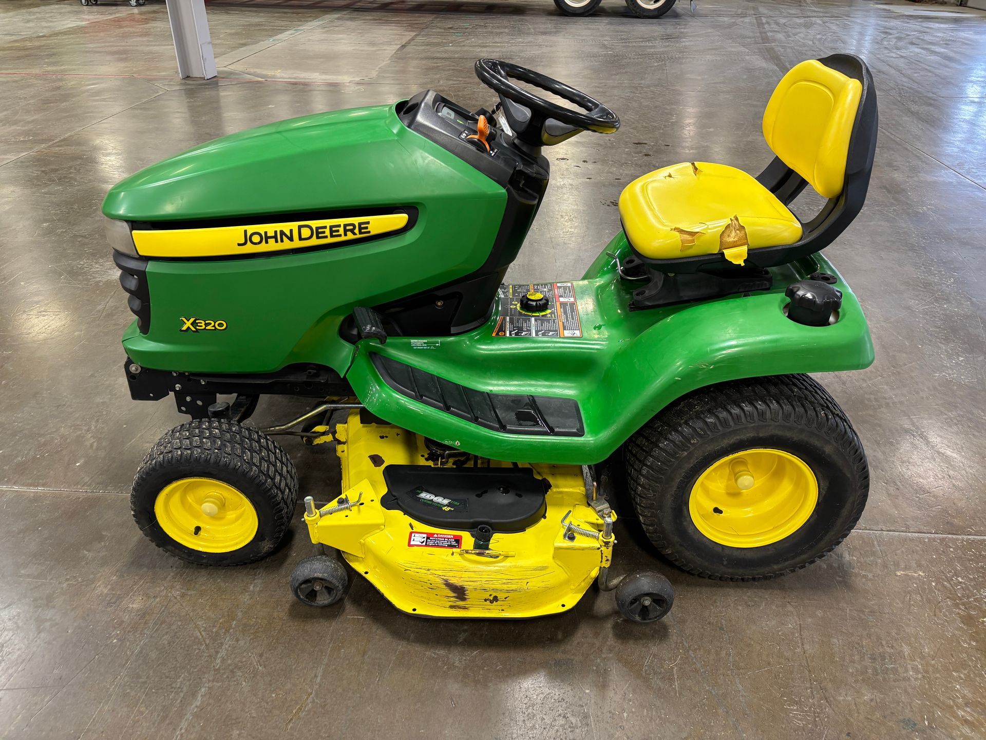 Green and yellow John Deere riding lawn mower, parked on a concrete surface.