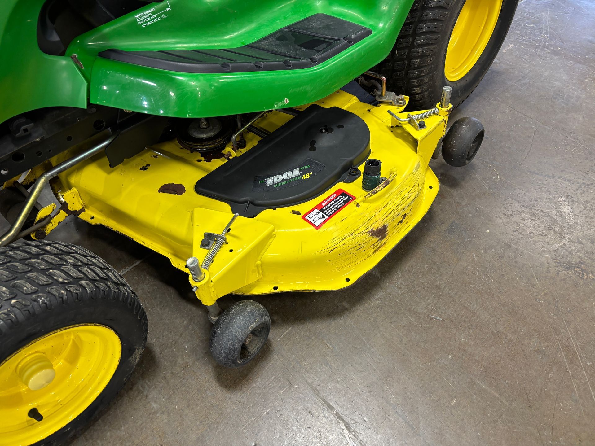 Yellow and green John Deere riding lawn mower, grass cutting deck in view.