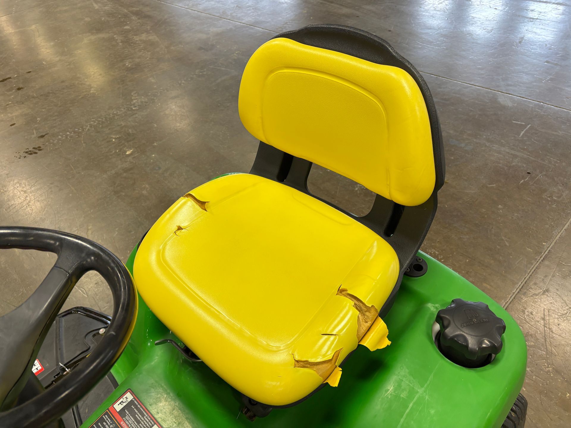 Yellow and black riding mower seat with cracked seat cushion.