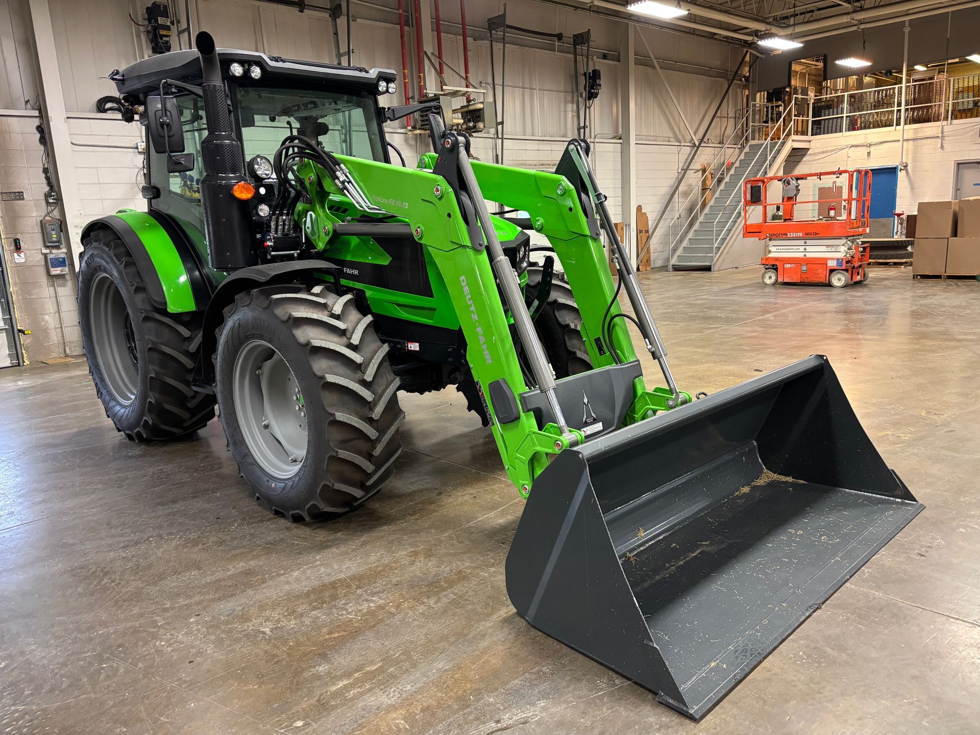 Green tractor with front-end loader in a warehouse setting.