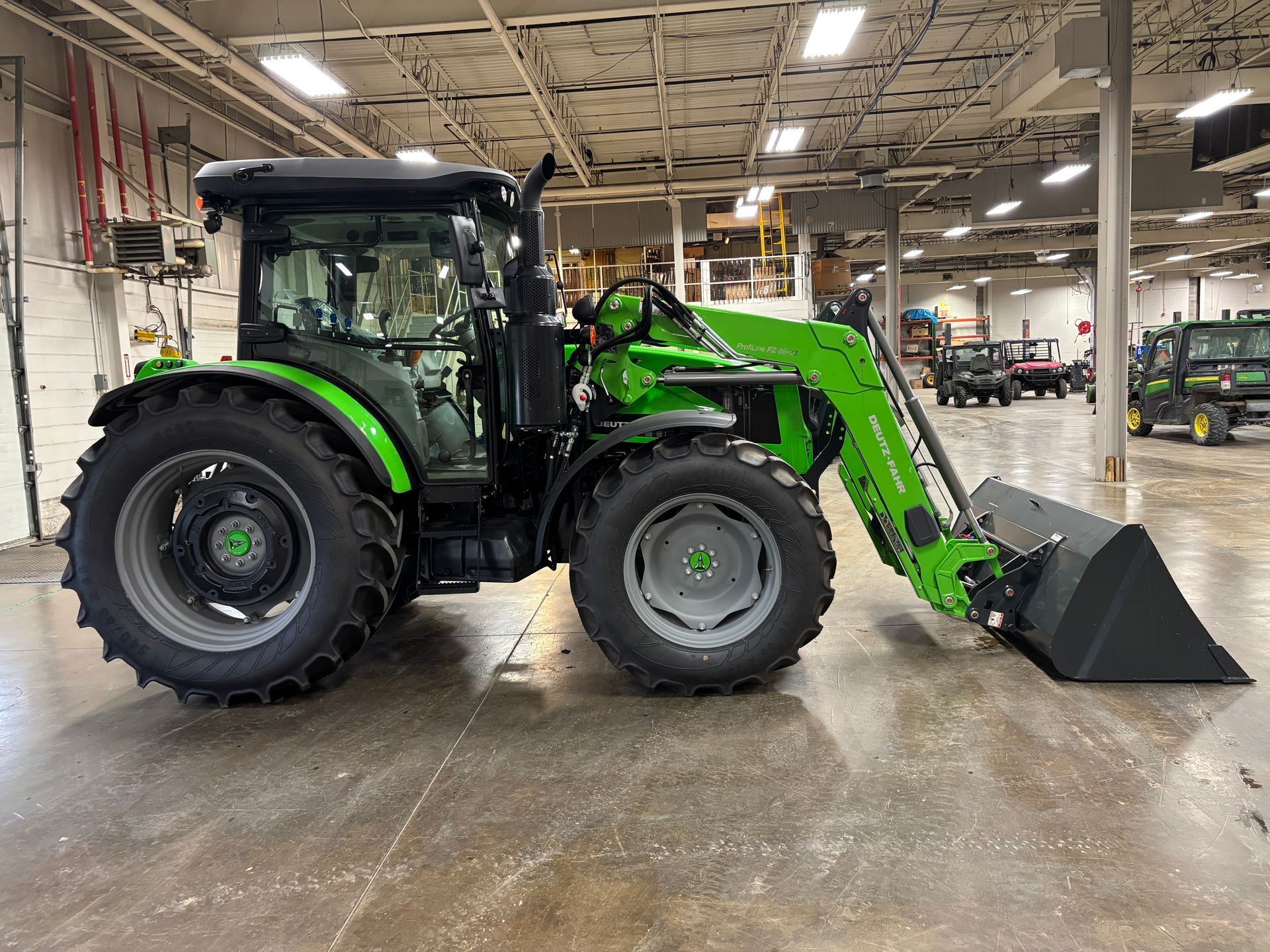 Green and black tractor with front loader inside a warehouse.