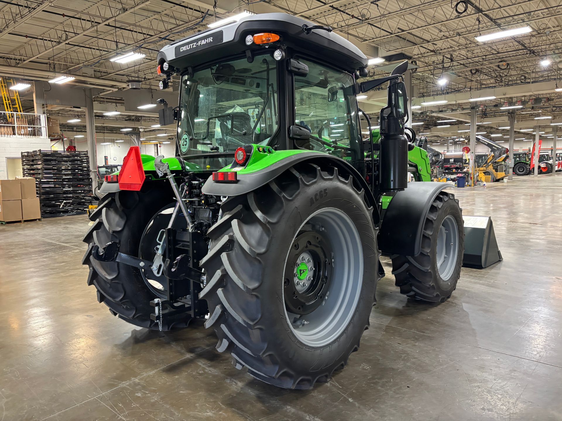 Green and black tractor with large tires inside a warehouse.