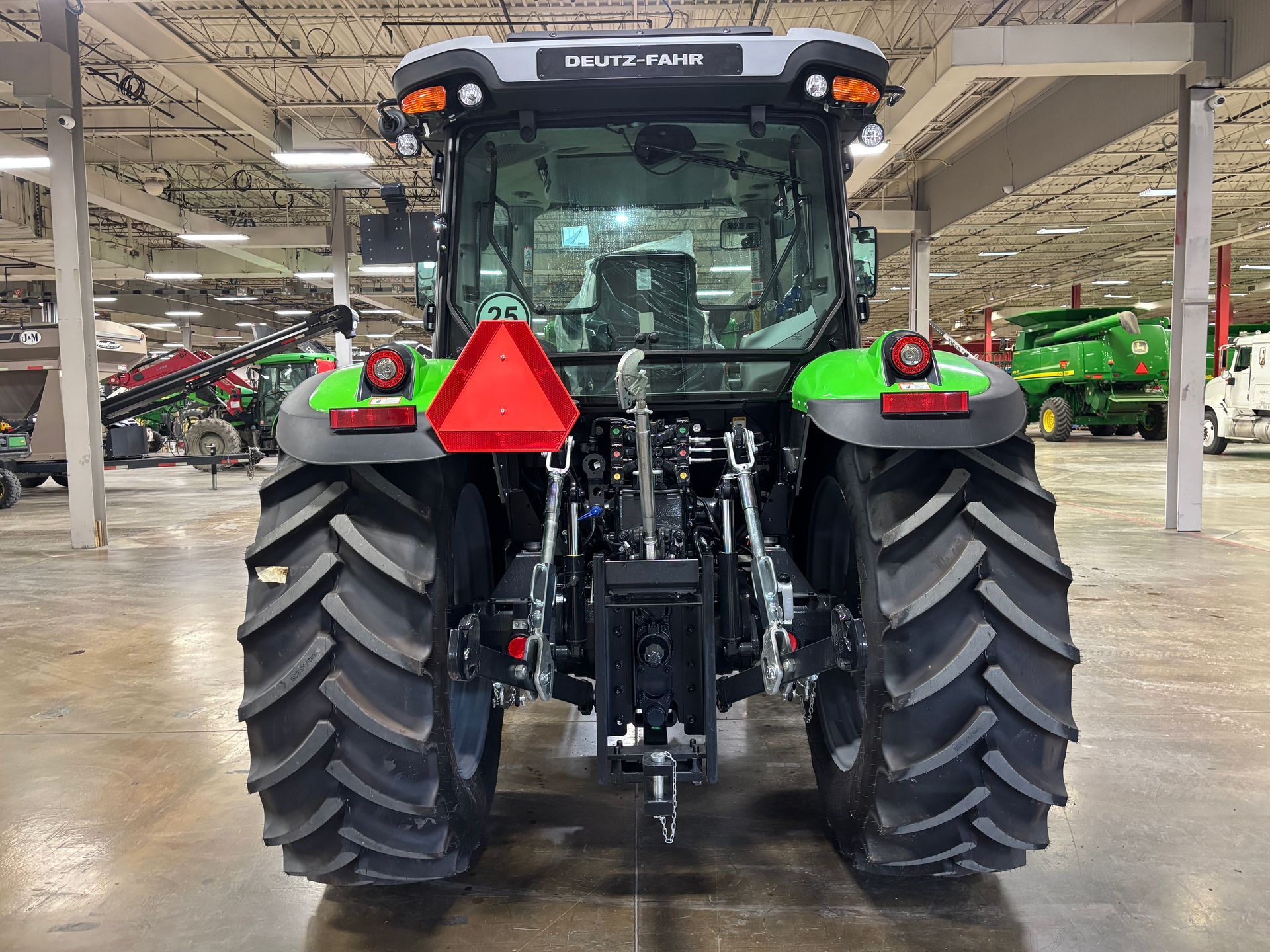 Rear view of a green and gray tractor with large tires, in a warehouse setting.