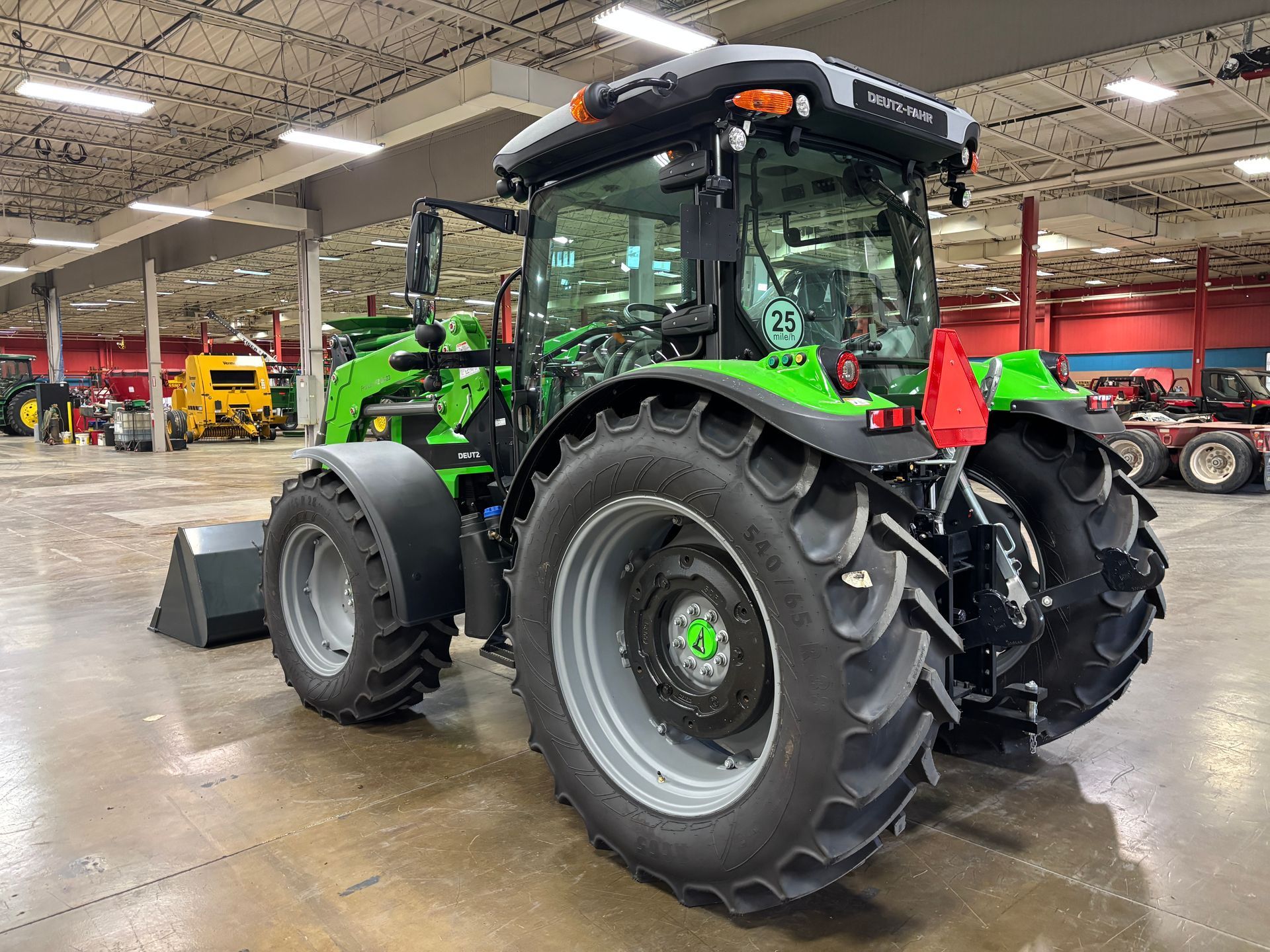 Green tractor with black cab and large tires, parked indoors.