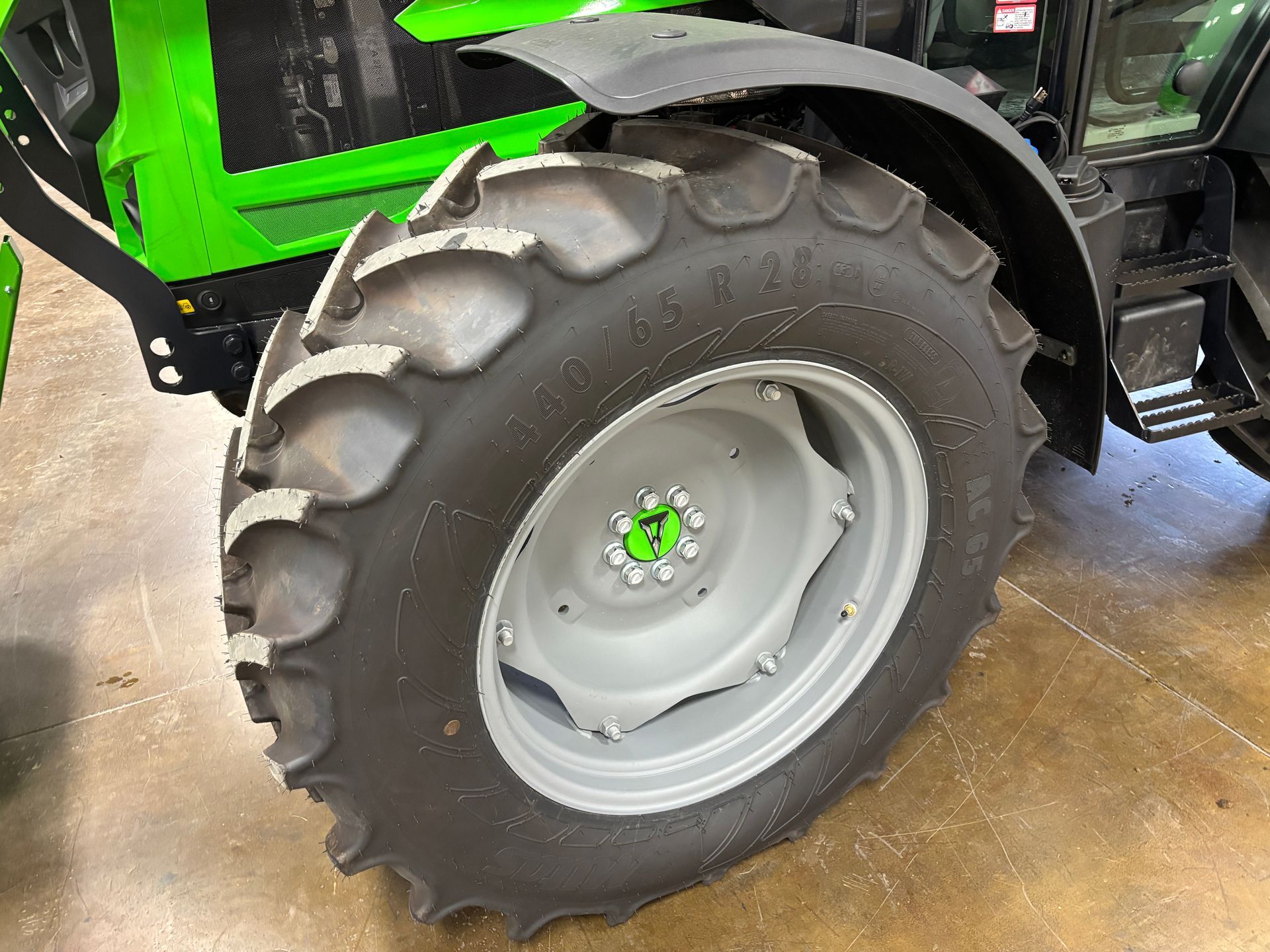 Close-up of a tractor tire with black tread and a gray wheel; part of the tractor is green.