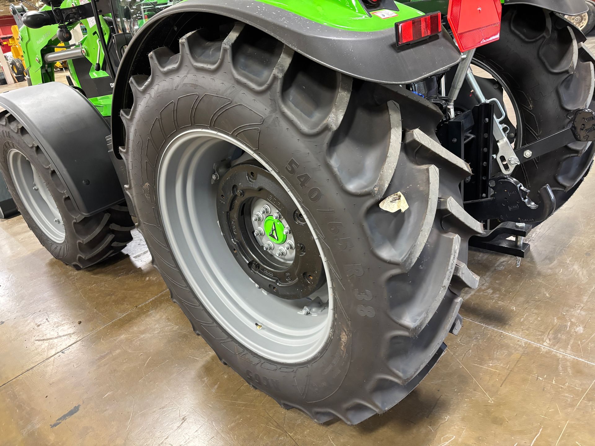 Close-up of a tractor's rear wheel and fender. The tire is black with deep treads, mounted on a gray rim.