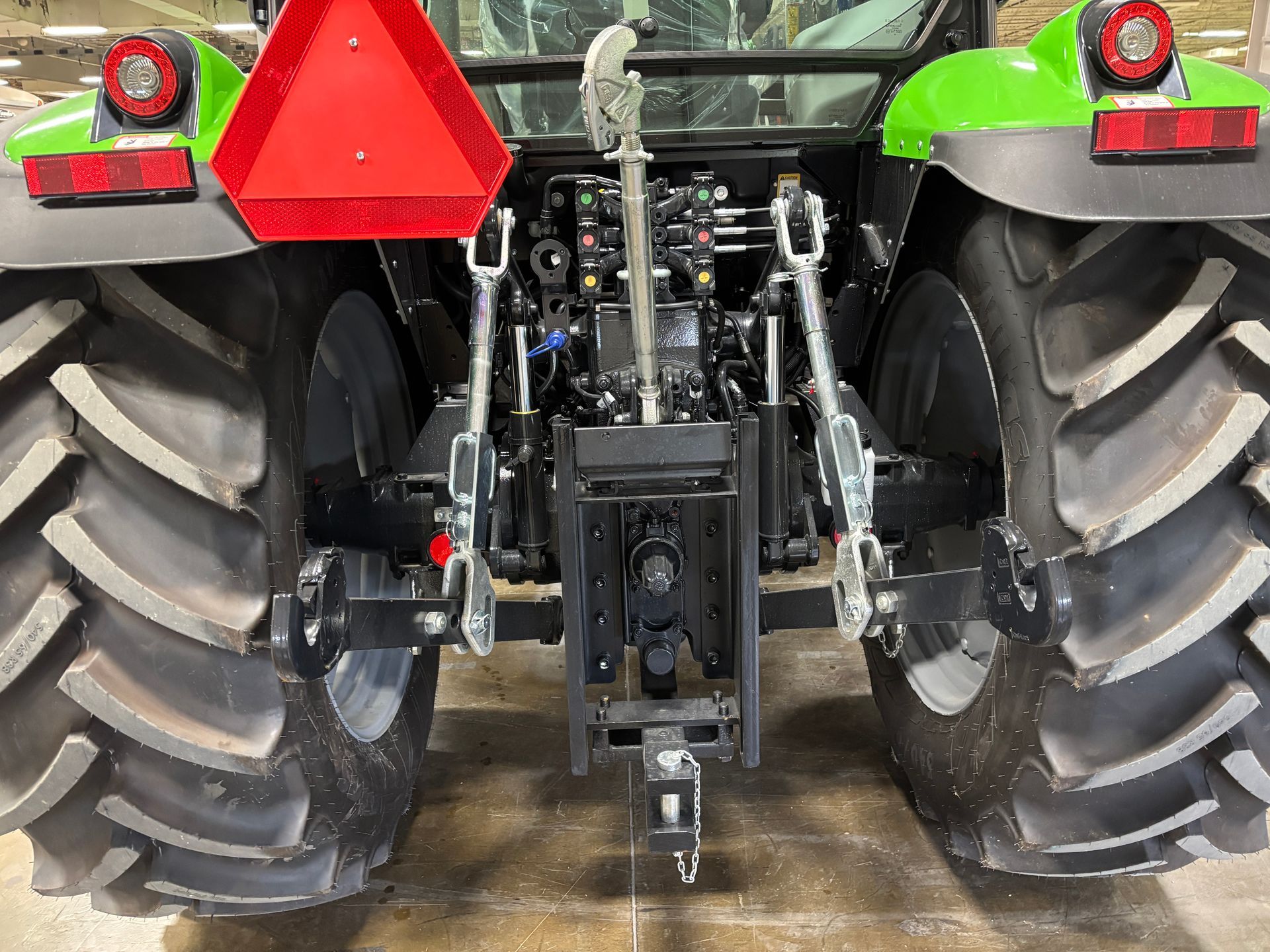 Rear view of a green and black tractor with large tires, a red triangle, and hitching components.
