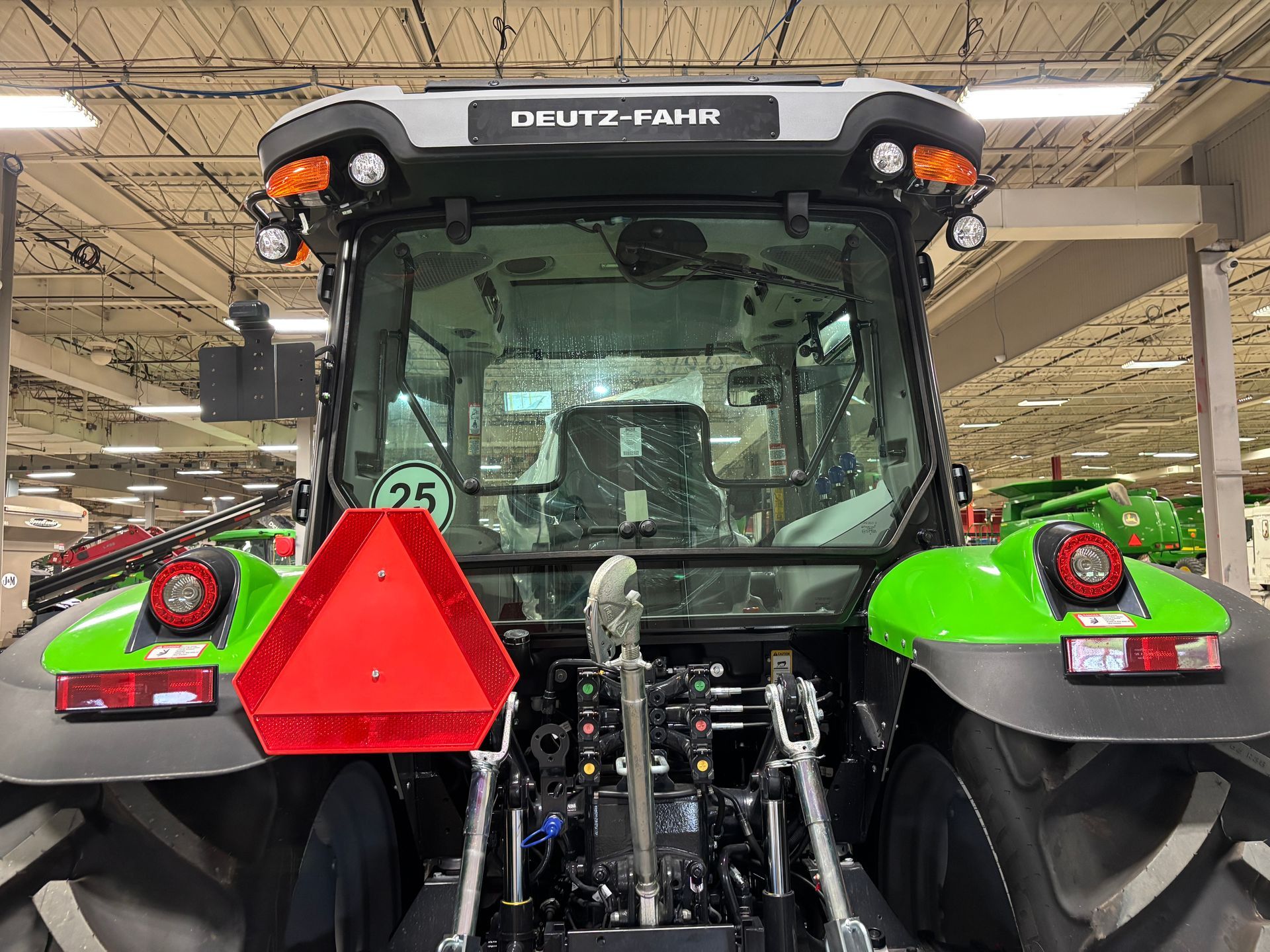 Rear view of a Deutz-Fahr tractor with a green and black body. A large red triangle and rear lights are visible.