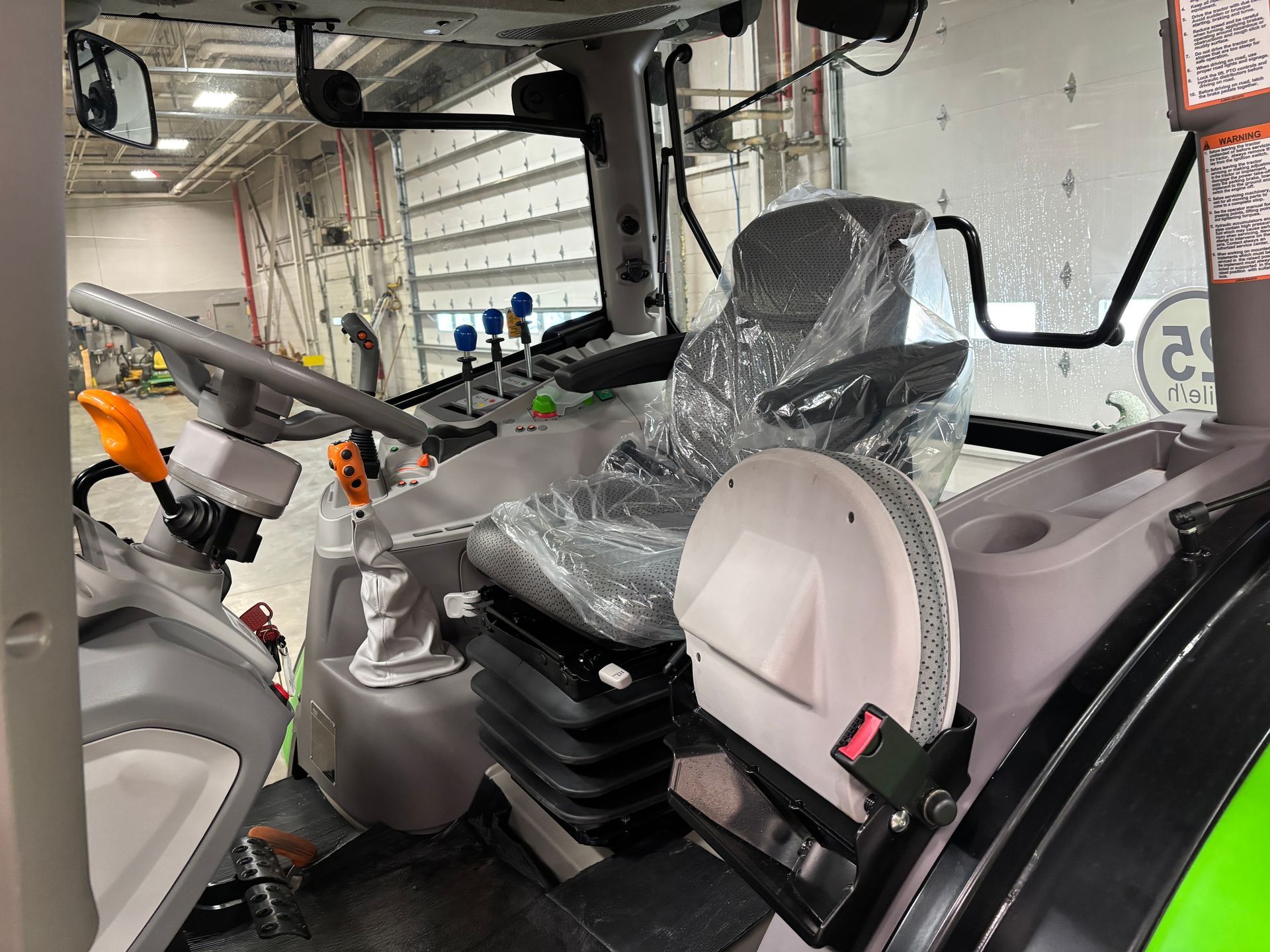 Interior of a tractor cab with protective plastic on the seat. Gray and green interior with controls visible.