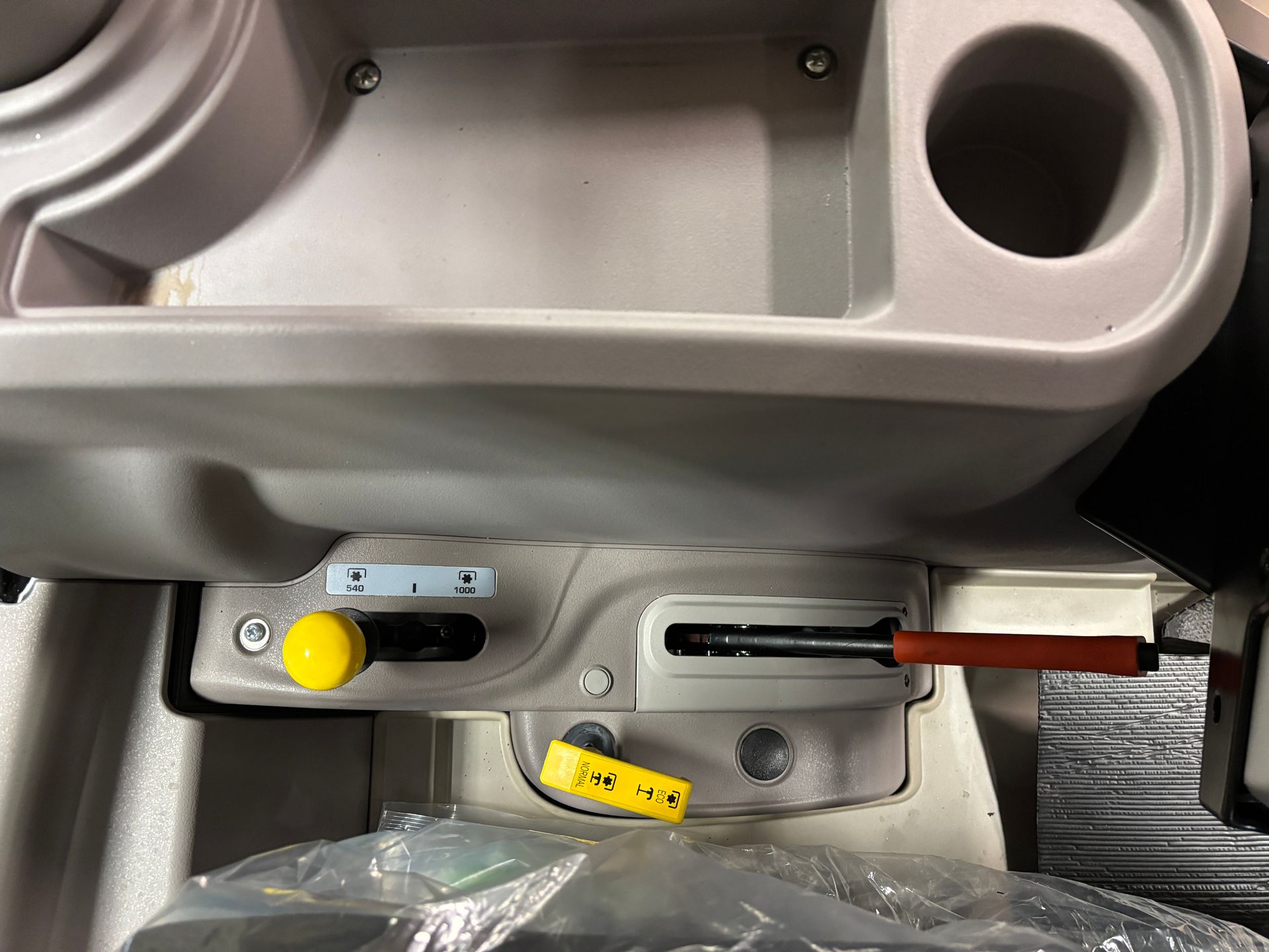 Close-up of tractor controls. Gray console with a yellow knob, black lever, and a red-handled sliding lever.