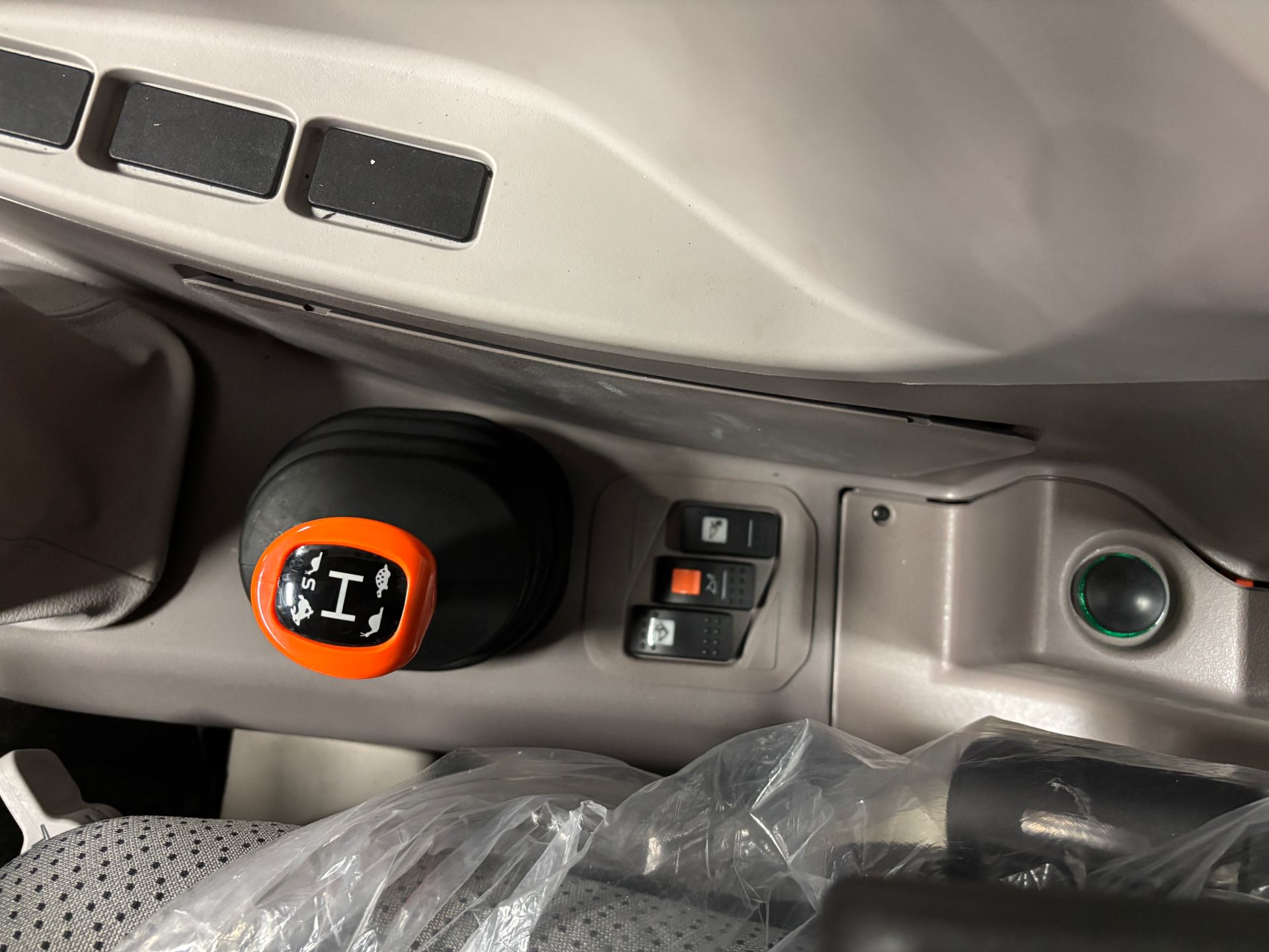 Orange and black gear shift lever in a tractor cab, with three black switches and a green light.