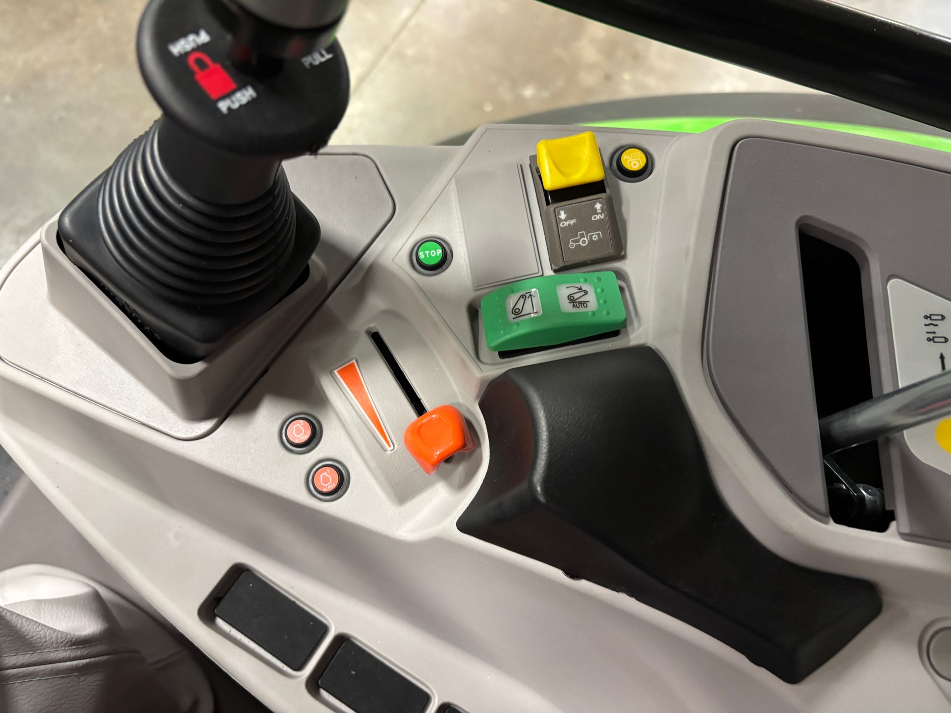 Control panel of a tractor with a joystick, levers, and various buttons in gray and green.