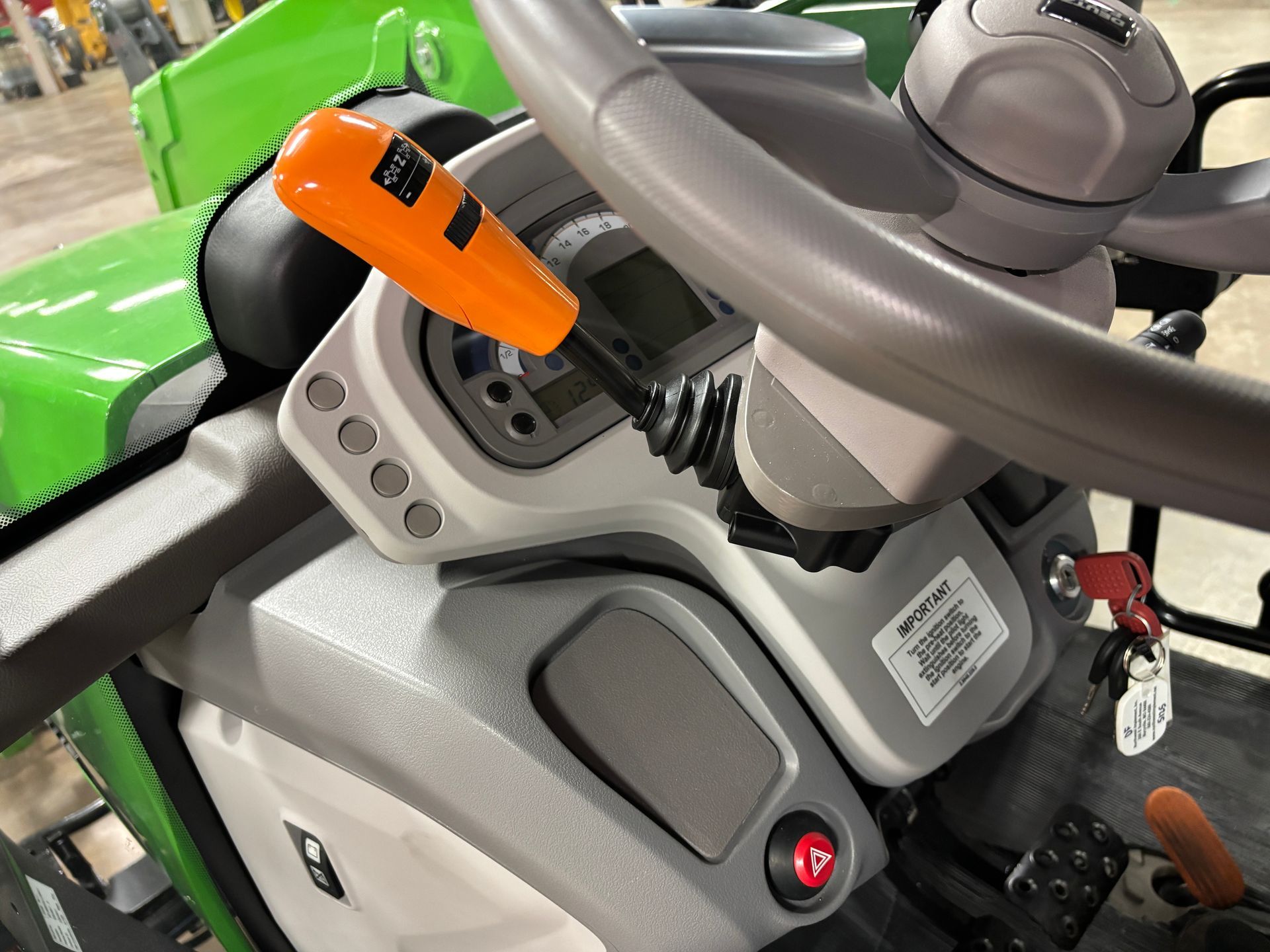 Tractor dashboard detail with steering wheel, orange lever, digital display, and gray and green interior.