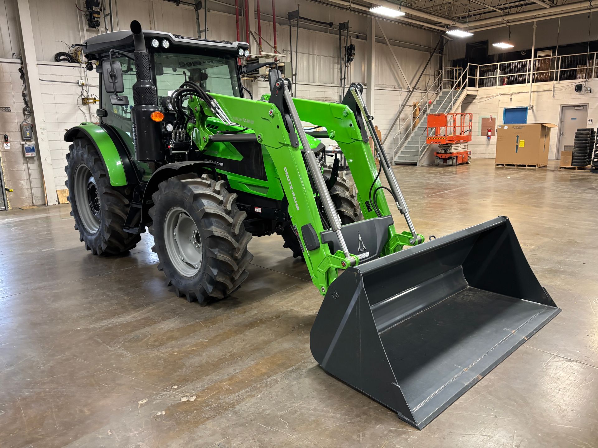 Green tractor with front loader inside a warehouse.