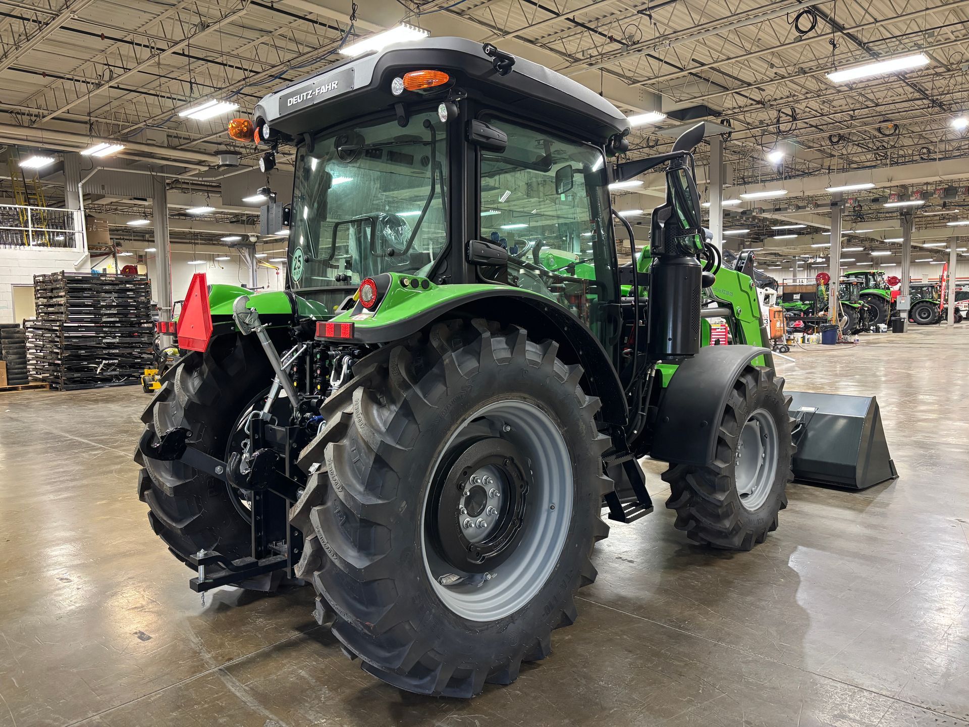 Green tractor with a cab, black fenders, and large rear tires inside a warehouse.