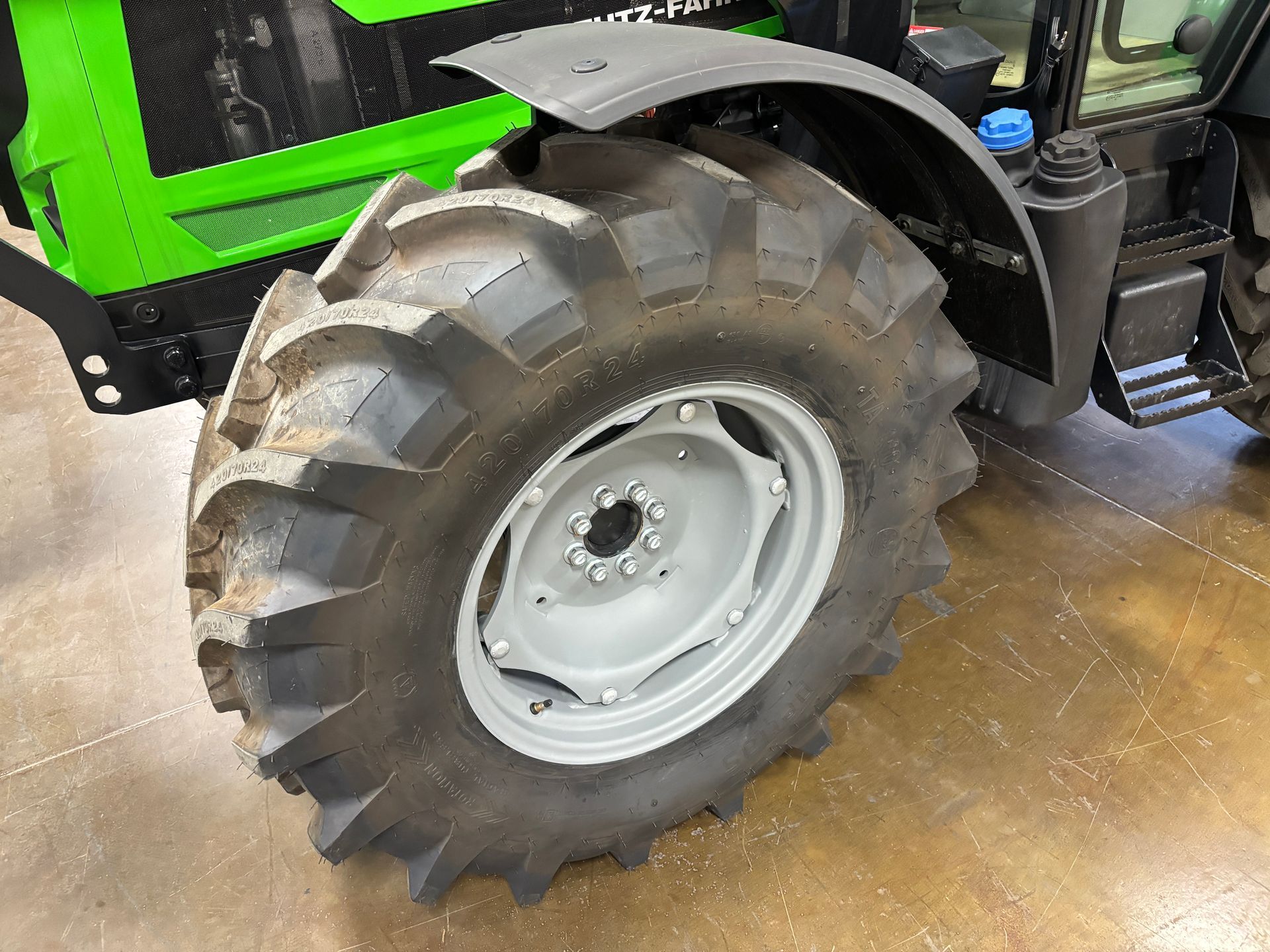 Black and green tractor tire and wheel, with a dark fender, and part of the tractor body.