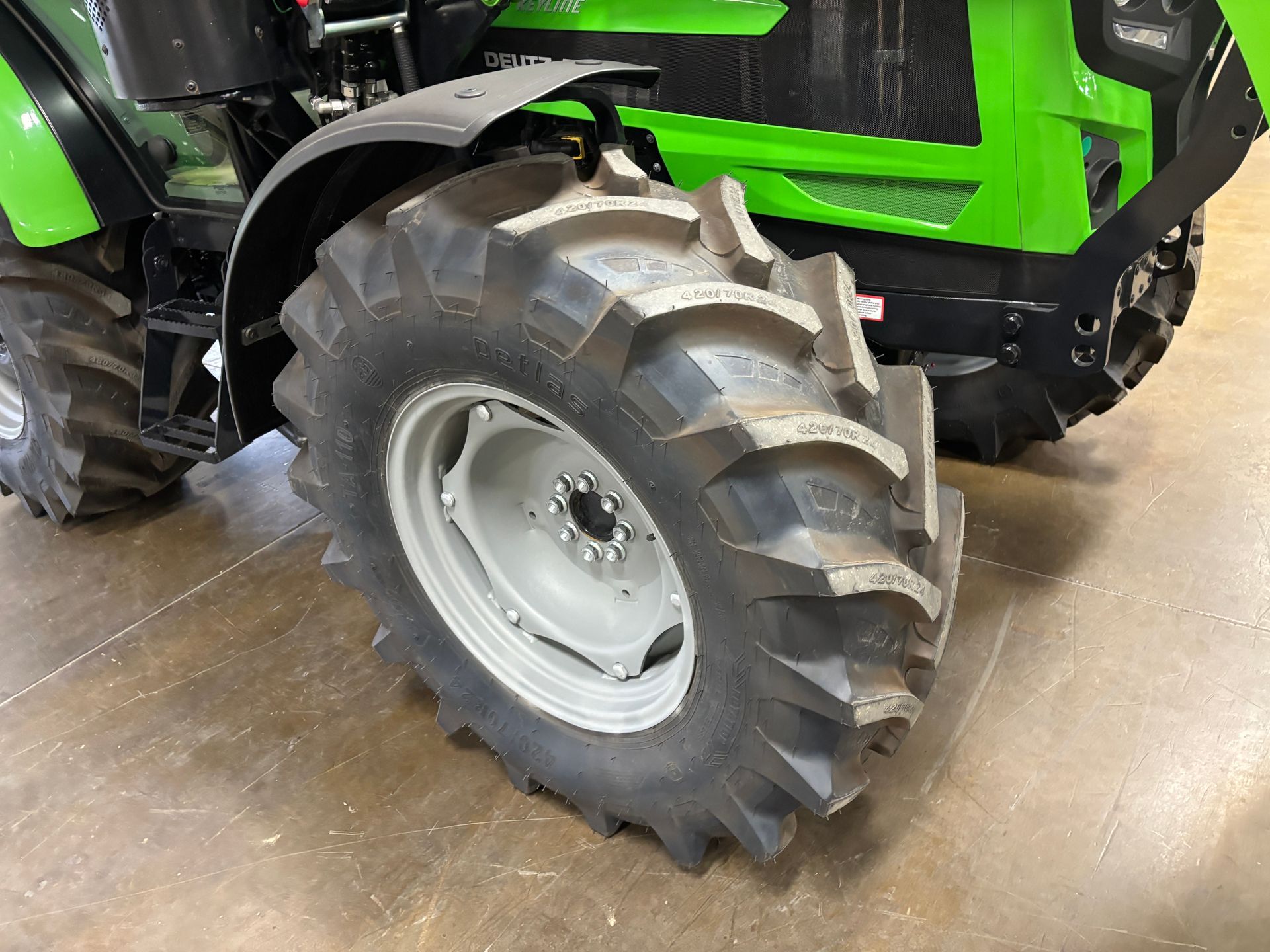 Tractor's large tire and wheel, with the green and black body visible in the background.