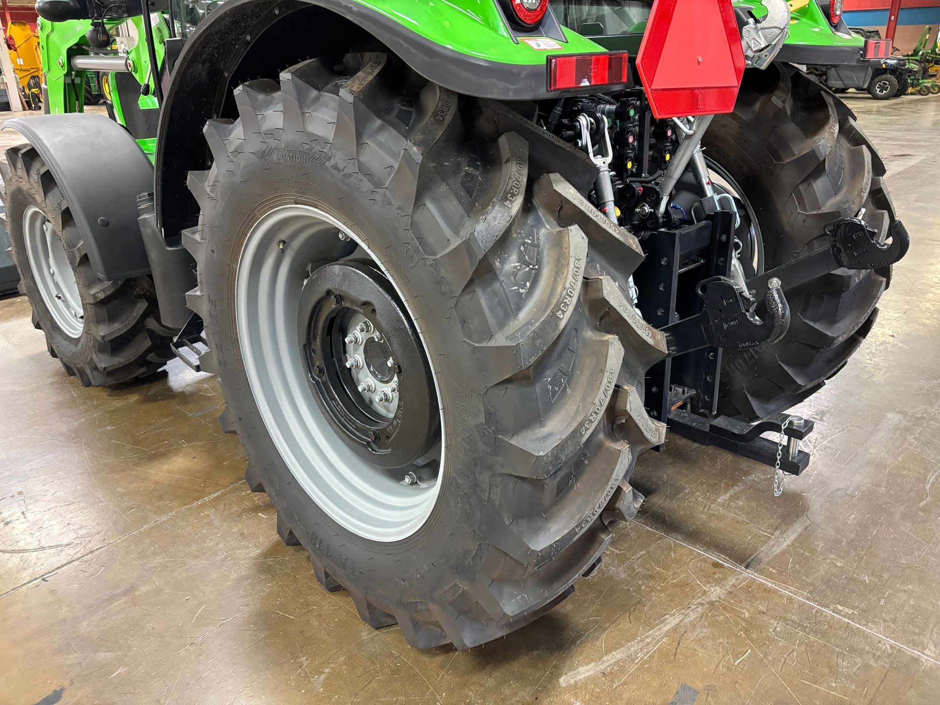 Close-up of a green tractor's rear tires and hitch. The tires have thick treads, and are on a gray rim.