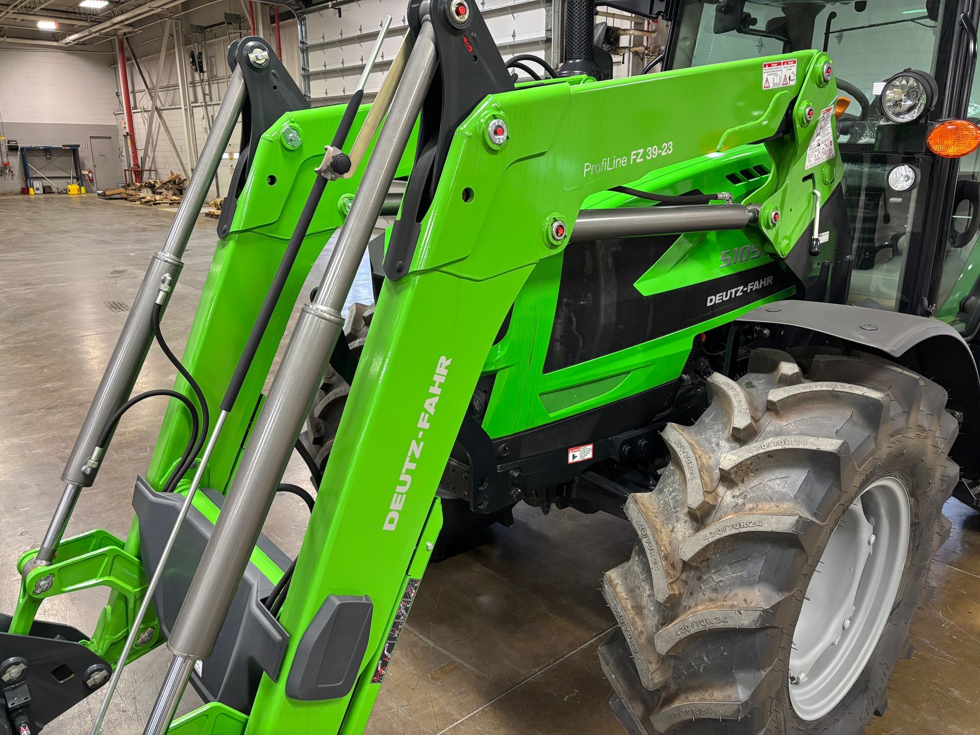 Green Deutz-Fahr tractor with loader attachment. Black accents, large tires, and interior setting.