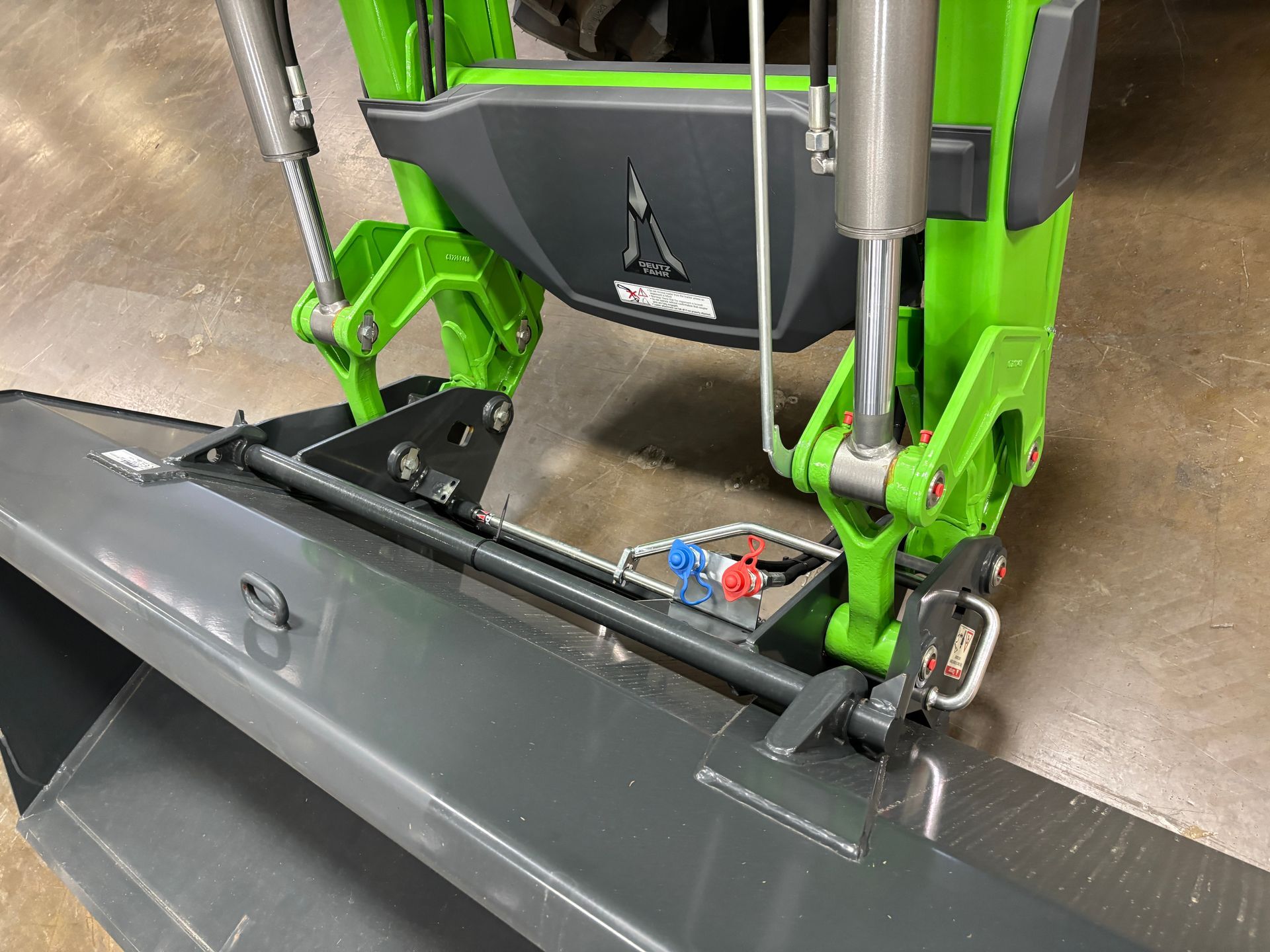 Green and gray tractor attachment. Hydraulic cylinders and hoses visible.