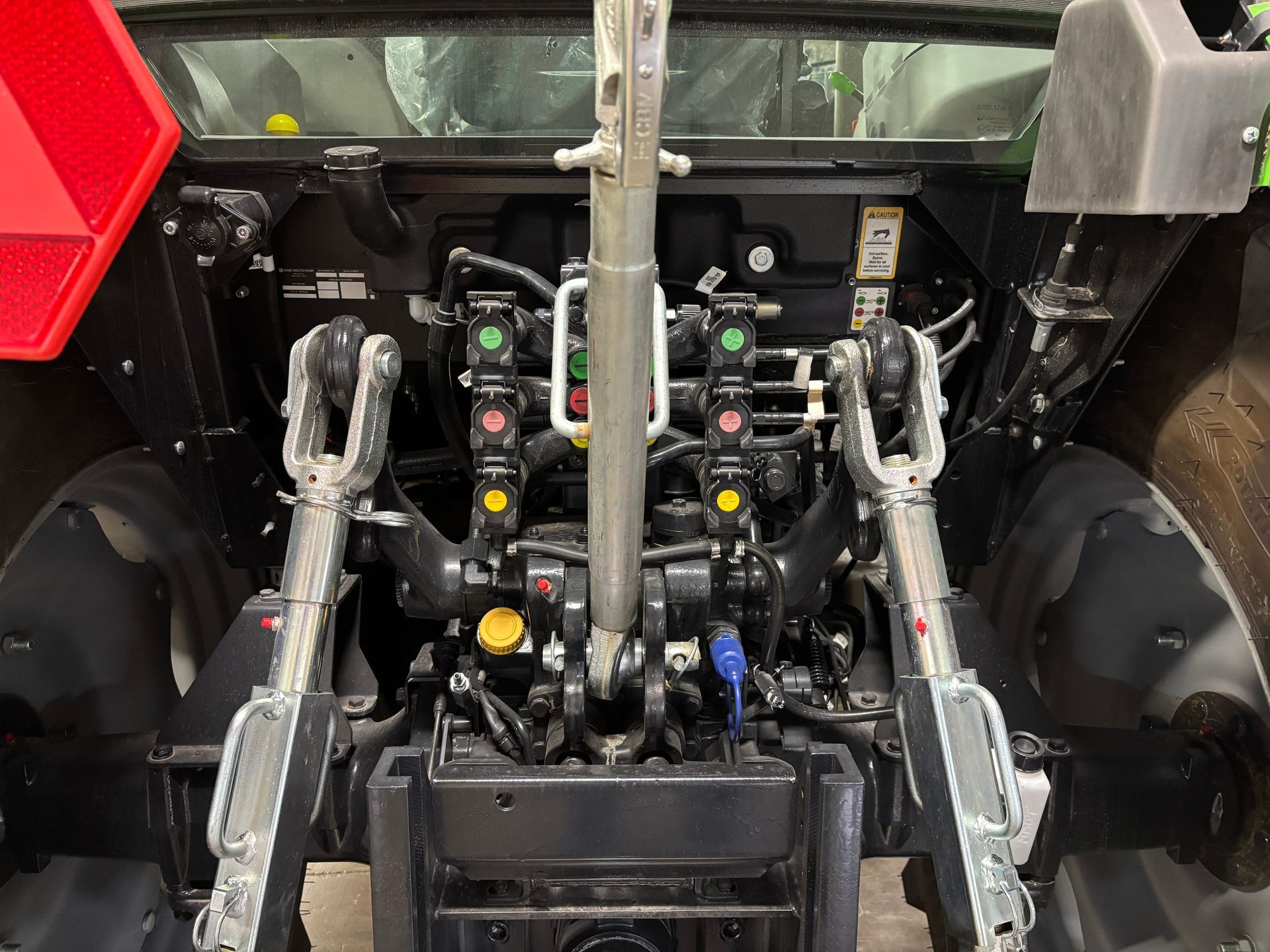 Rear of a green and black tractor showing hitch arms and hydraulic controls.