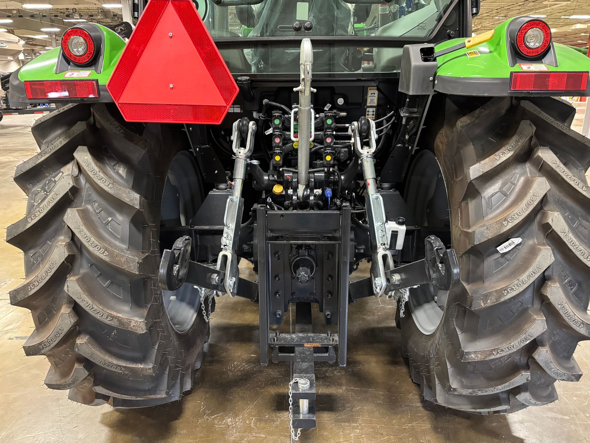 Rear view of a green tractor with large tires, hitch, and red warning triangle.