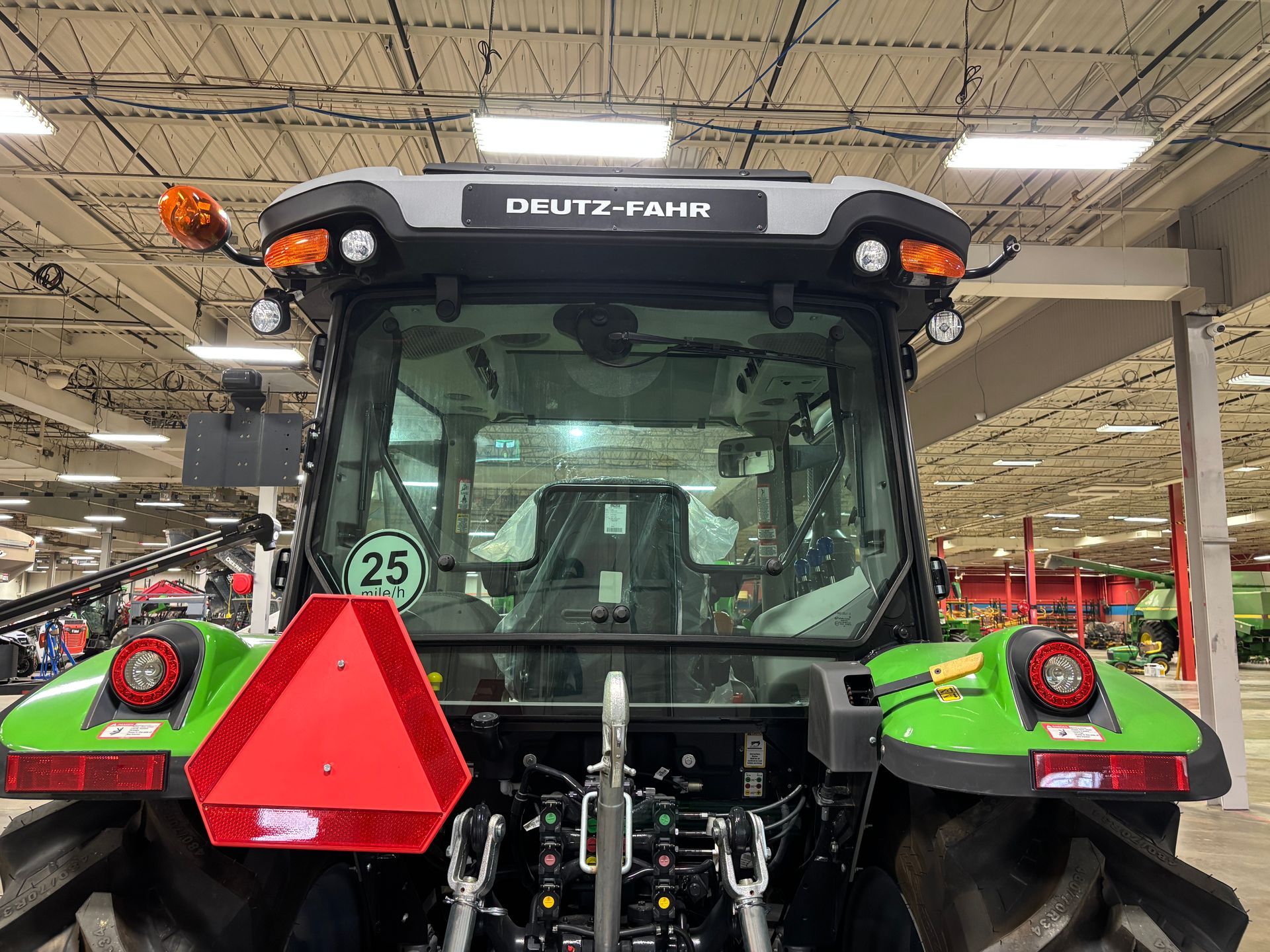 Rear view of a Deutz-Fahr tractor with green and black accents, a red triangle, and orange lights.