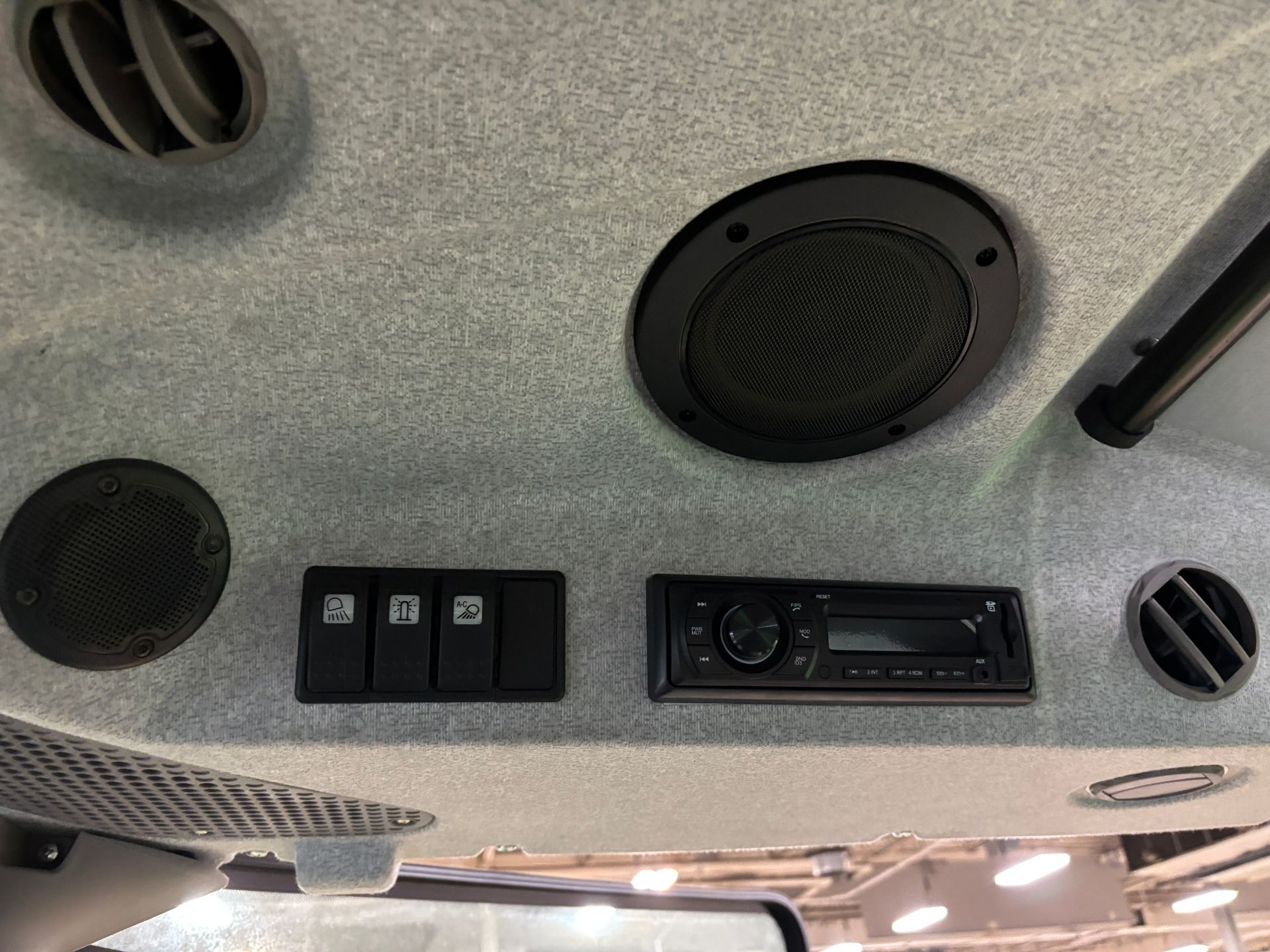 Interior tractor cab roof with speaker, radio, switches, and air vents. Gray fabric.