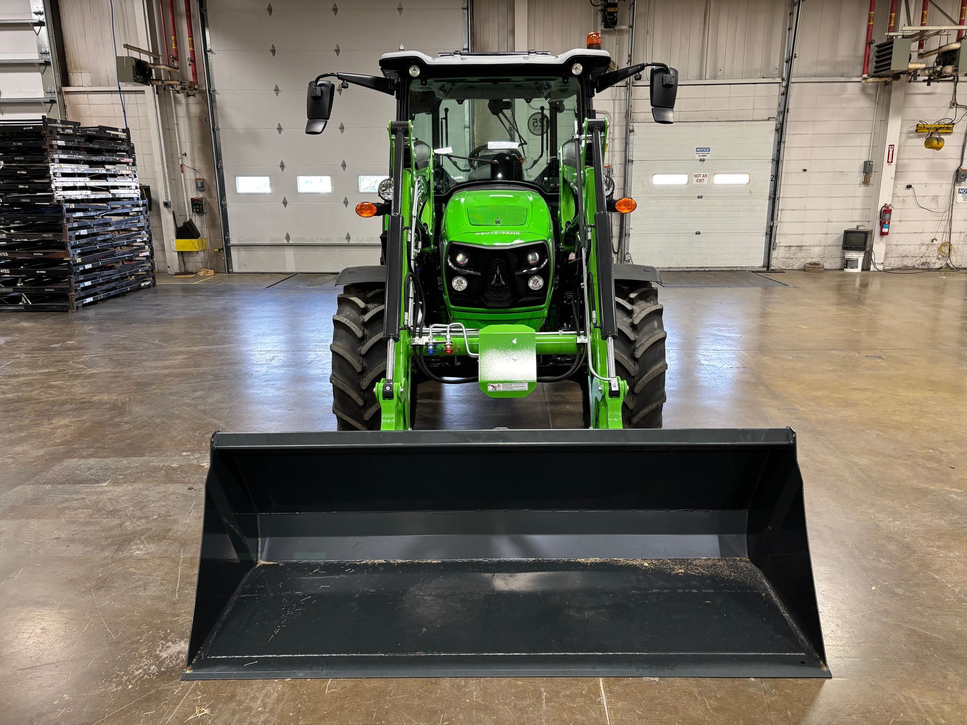 Green tractor with a front-mounted black bucket, parked indoors.