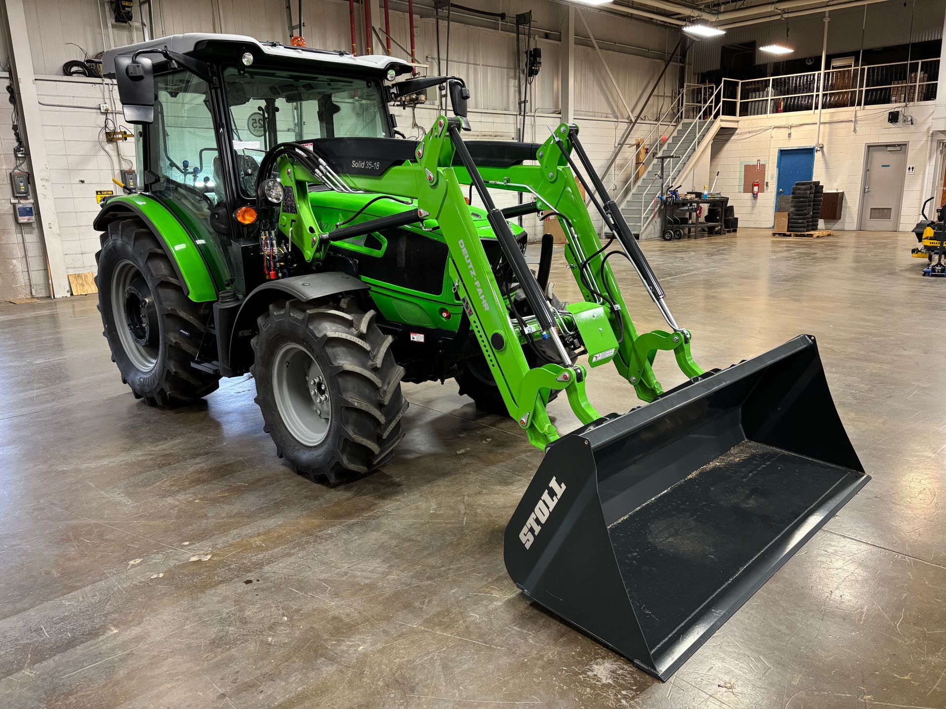 Green tractor with front loader in a warehouse.