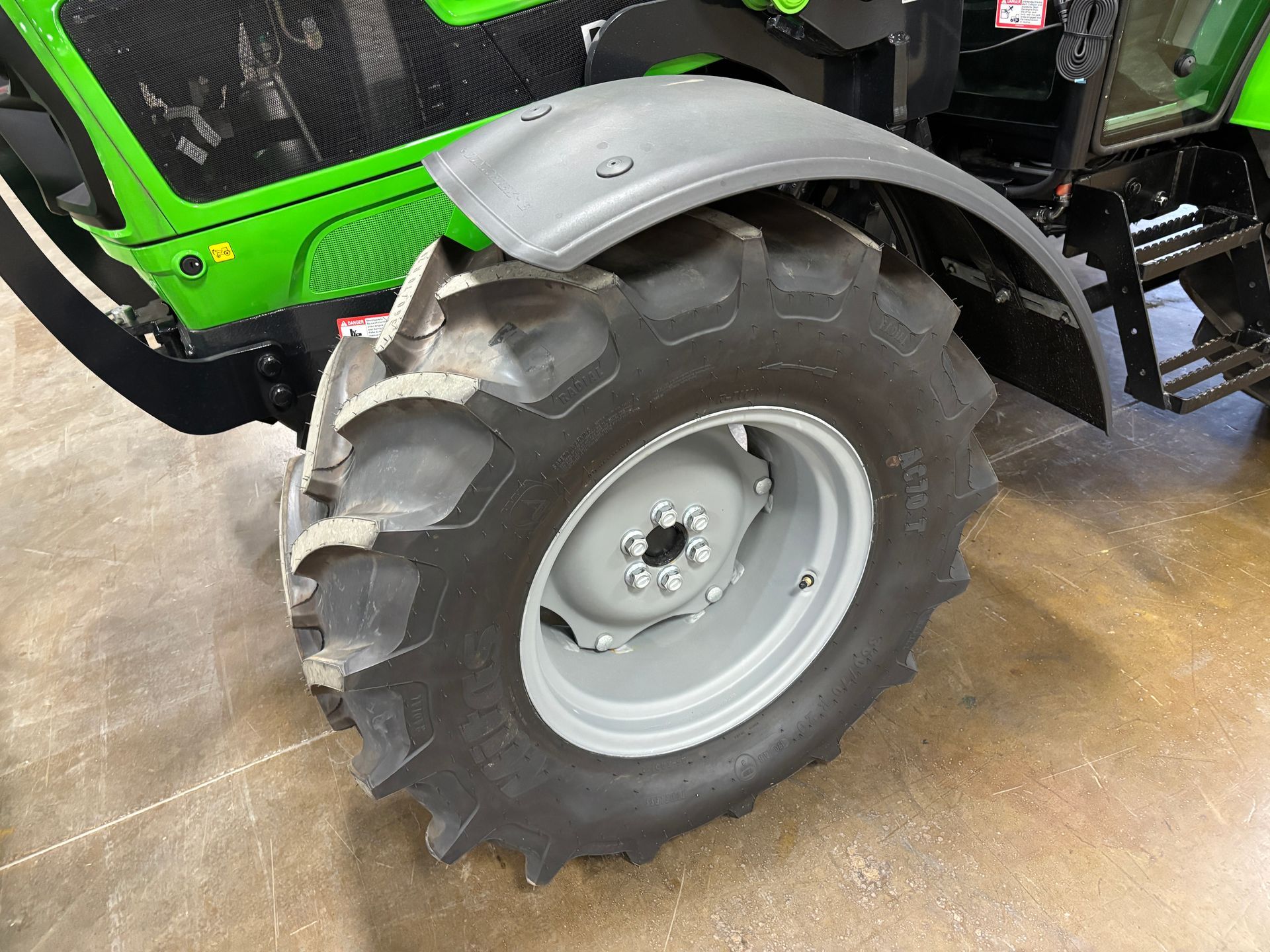 Close-up of a tractor's rear wheel with a gray rim, black tire, and green body panel.