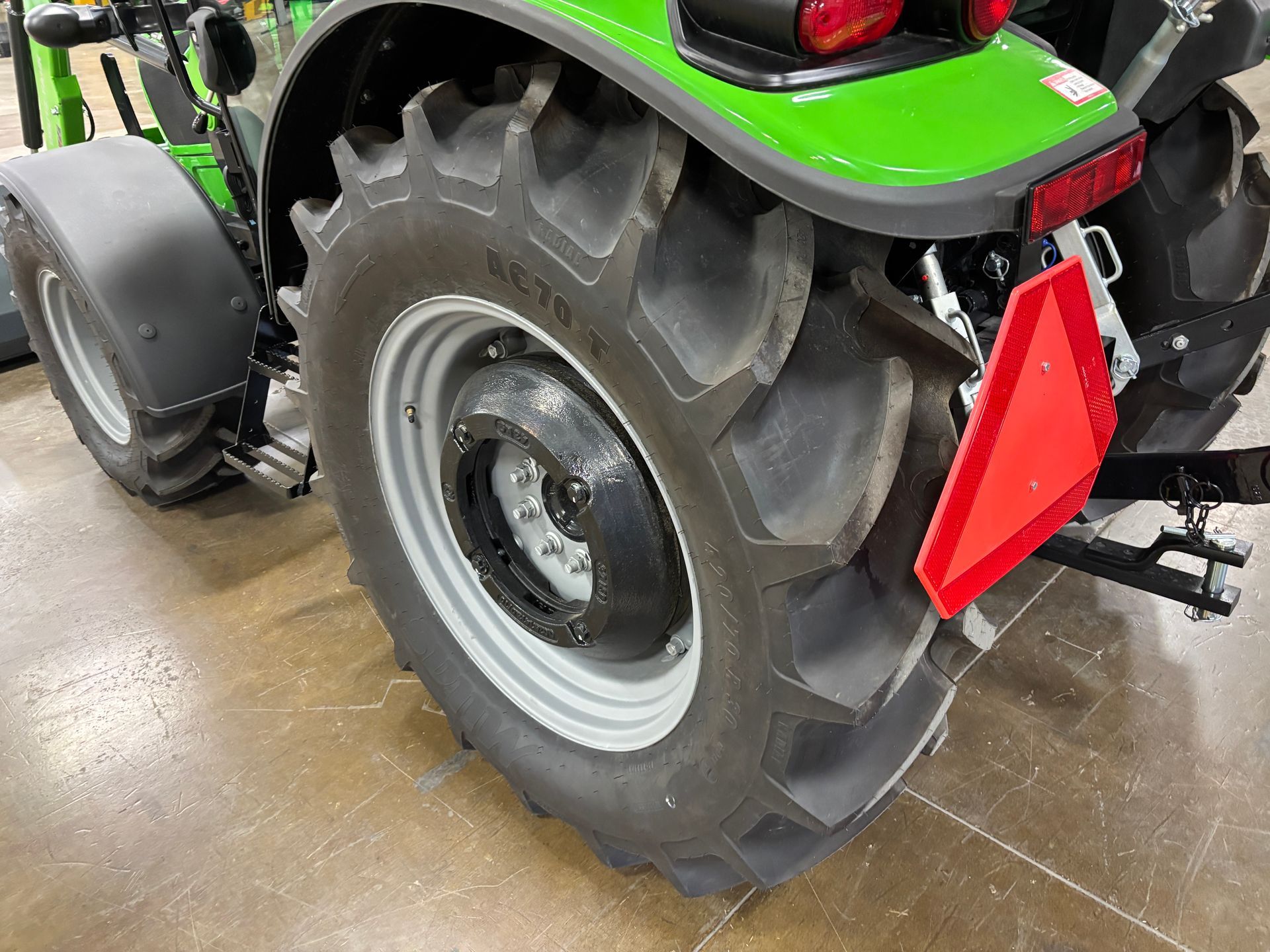 Green tractor rear tire with reflective triangle, likely in a showroom.