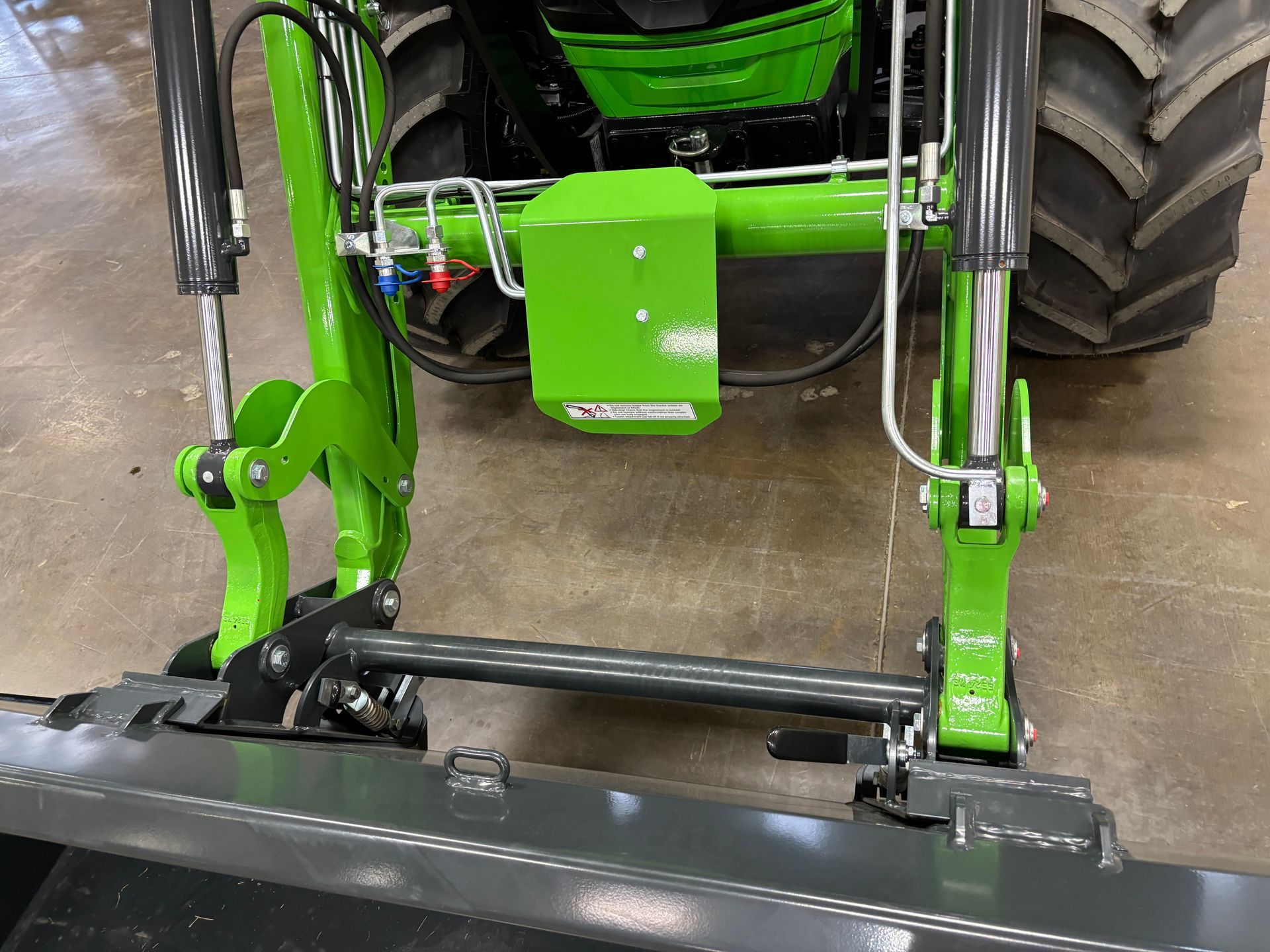 Green tractor front loader, metal bucket, hydraulic cylinders, close-up shot.