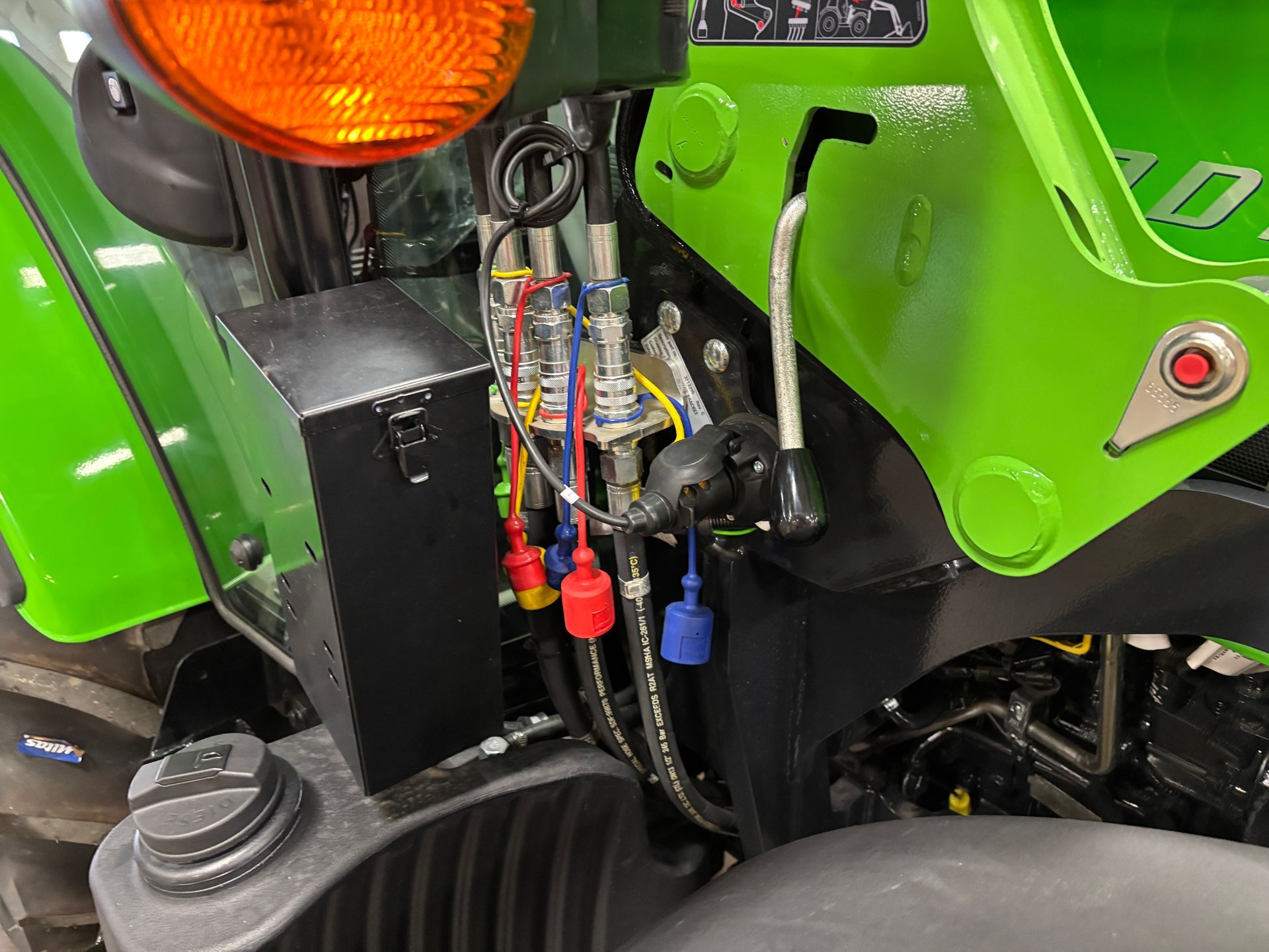 Close-up of a green tractor's hydraulic connections with colored plugs and a black metal box.