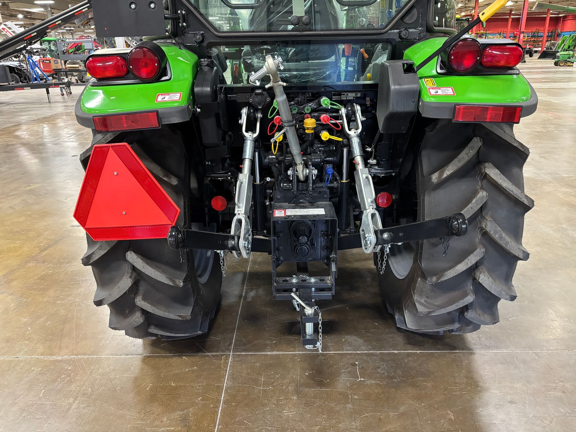 Rear view of a green tractor with large tires, hitch, and triangular warning sign.