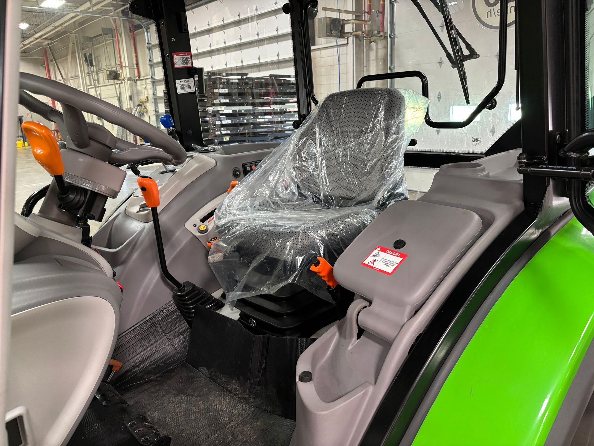 Interior view of a tractor cab with seat covered in plastic, steering wheel, and control levers.