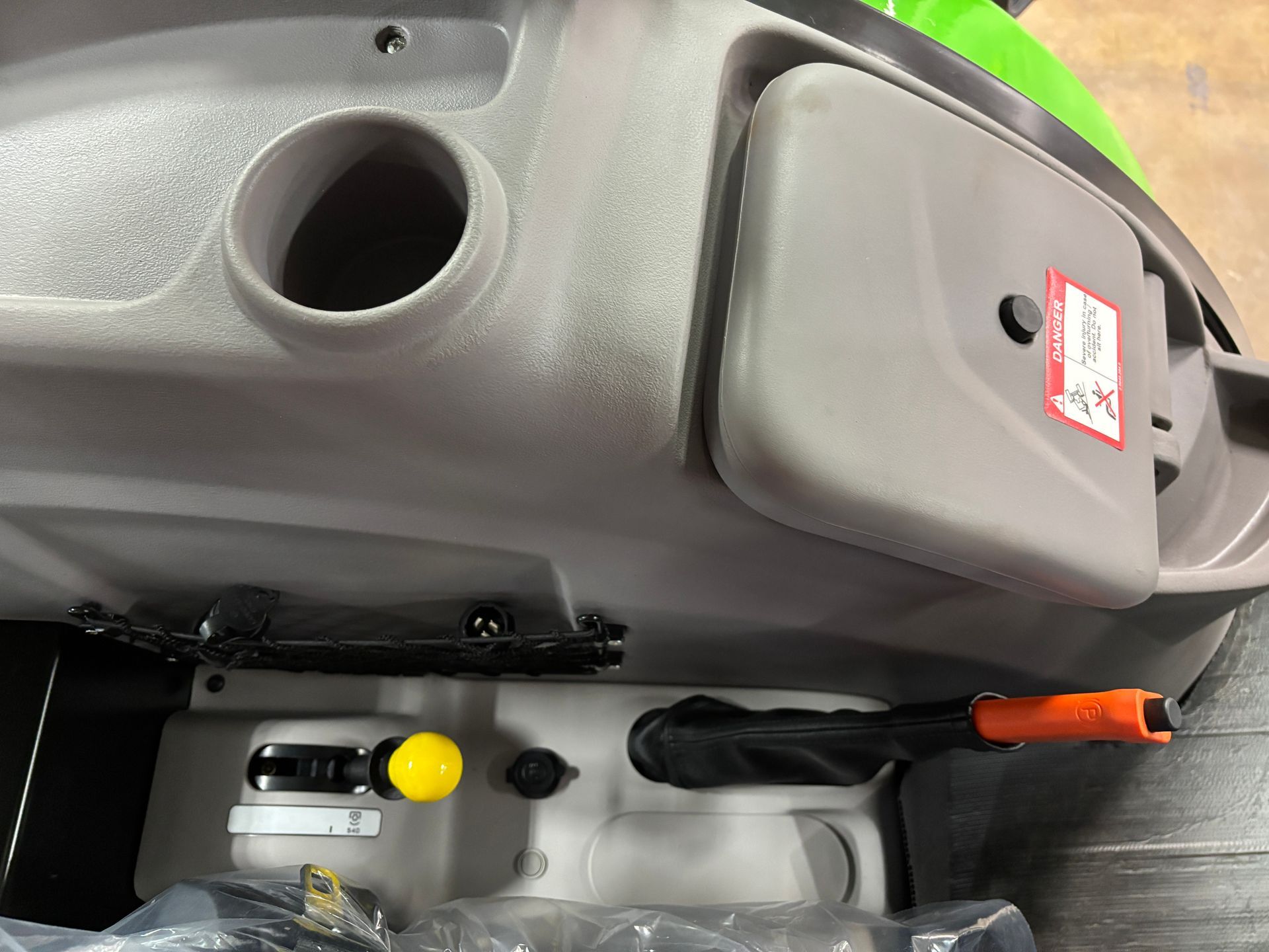 Gray tractor interior with cup holder, storage compartment, and lever controls.