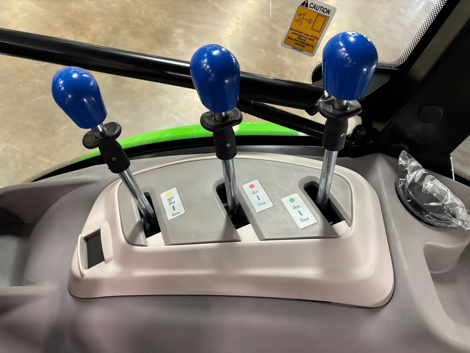 Three blue-handled levers on a tractor's dashboard, with labeled control positions, in a gray interior.