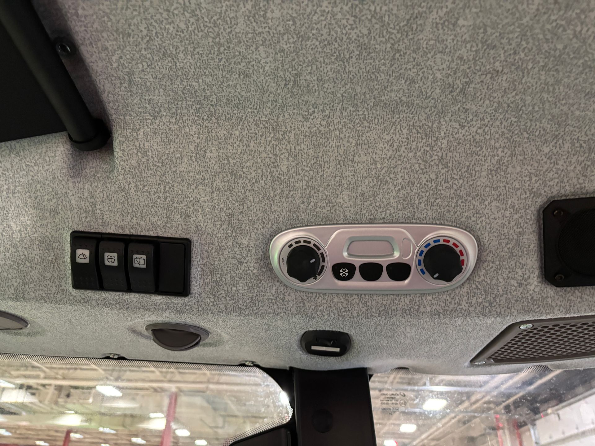 Interior of vehicle cab ceiling with control panel, switches, and air vents.