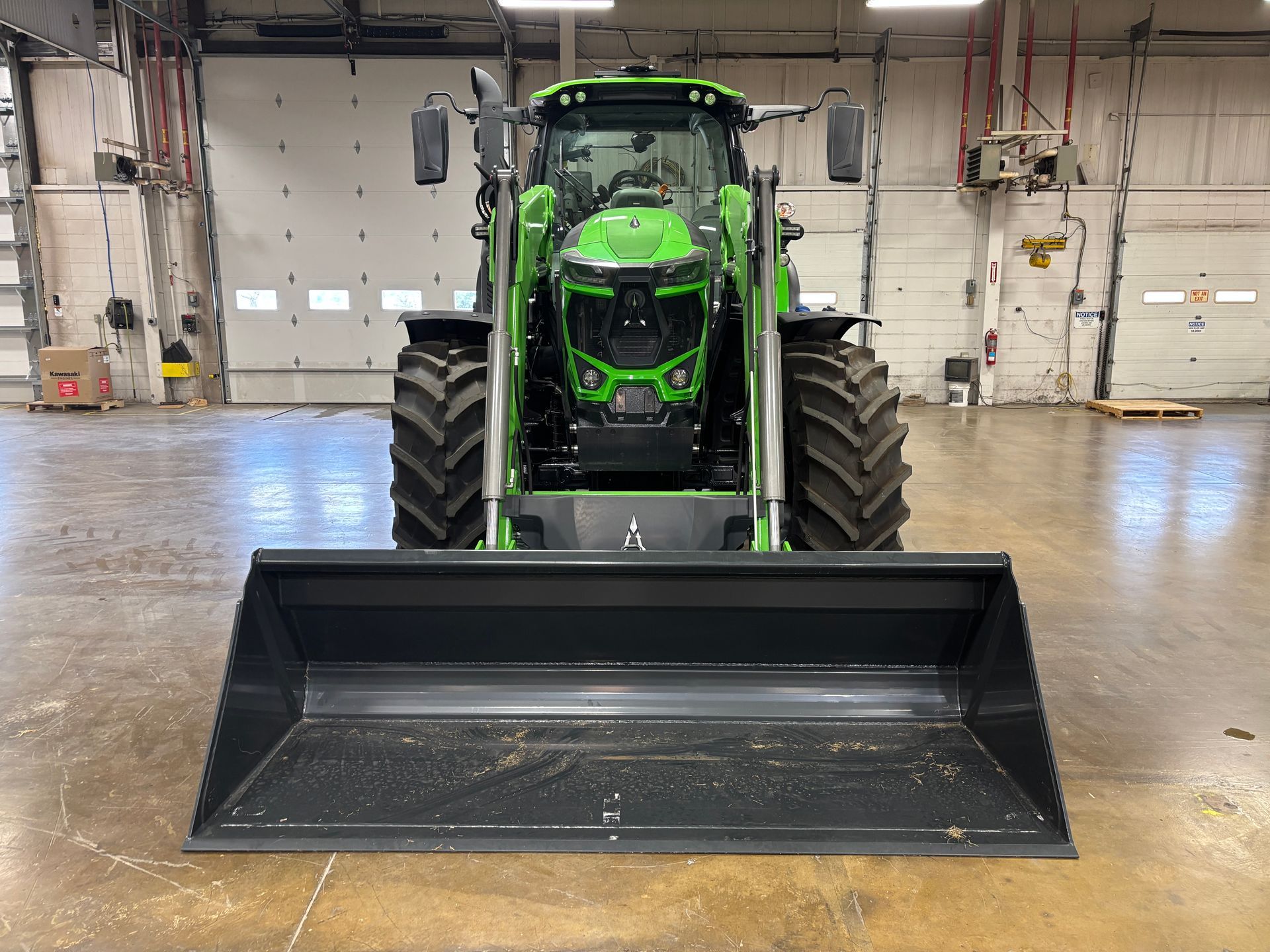 Green tractor with front loader in a warehouse.