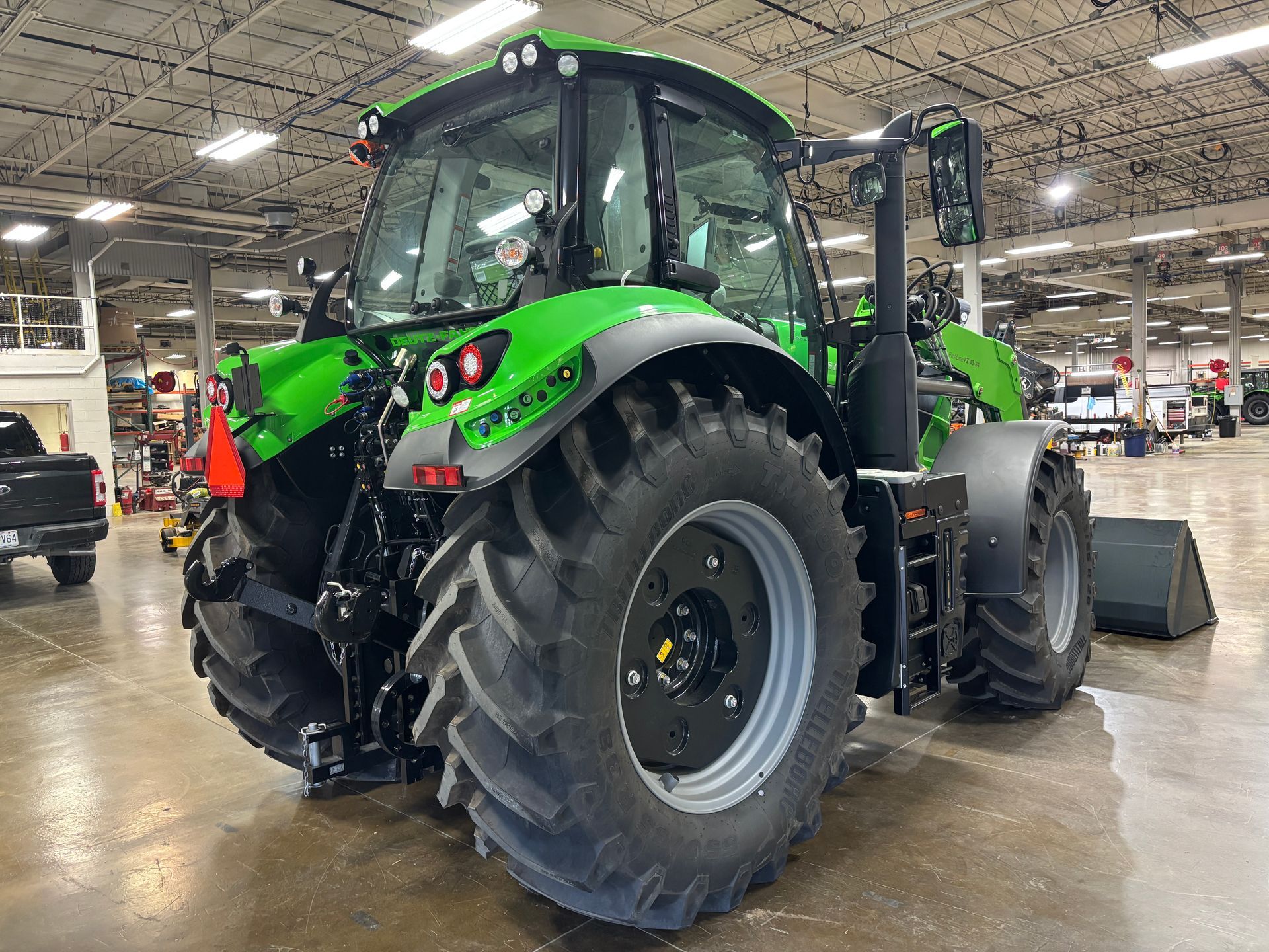 Green tractor, black tires, in a large warehouse.