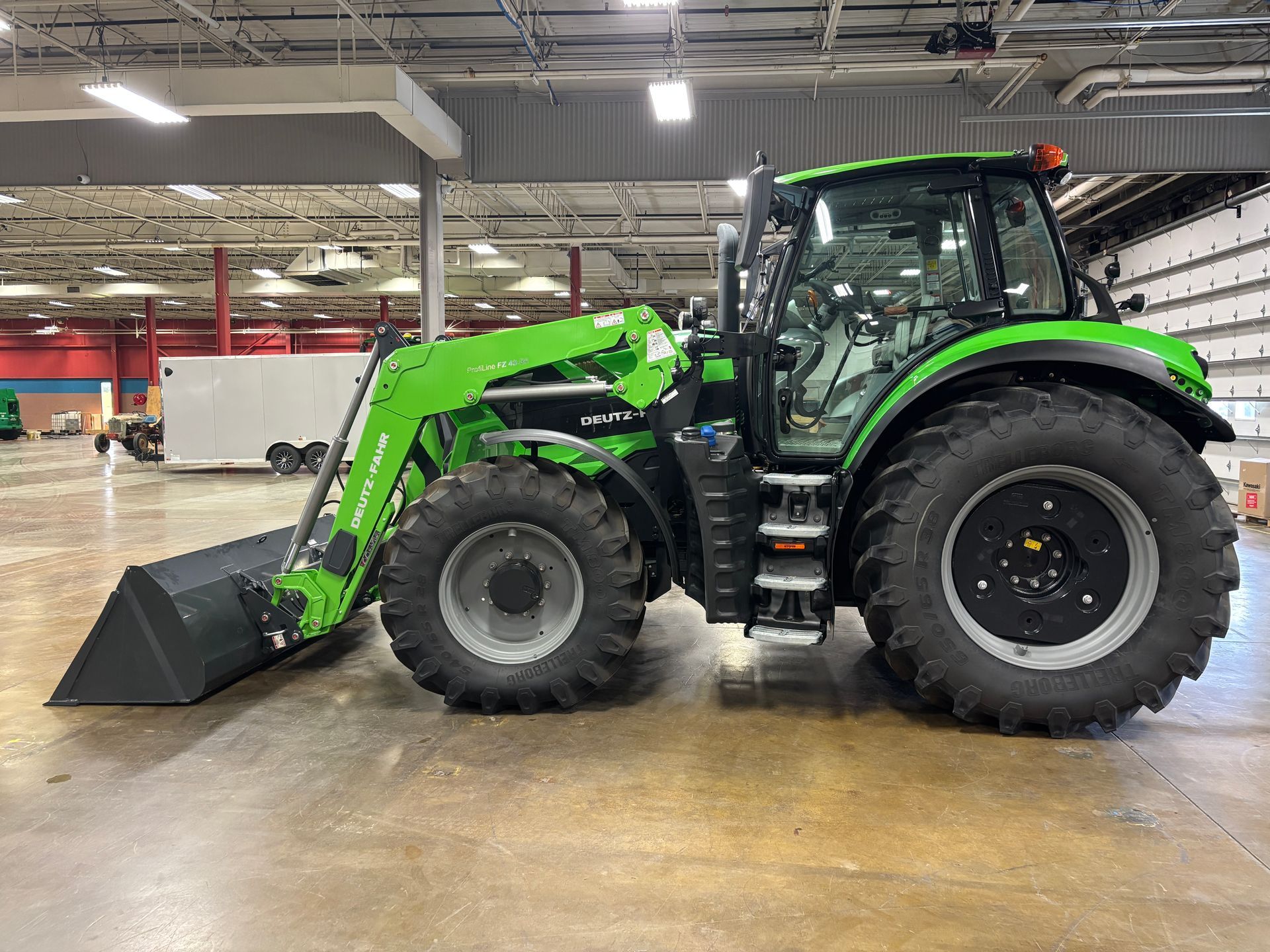 Green tractor with a front loader in a warehouse.