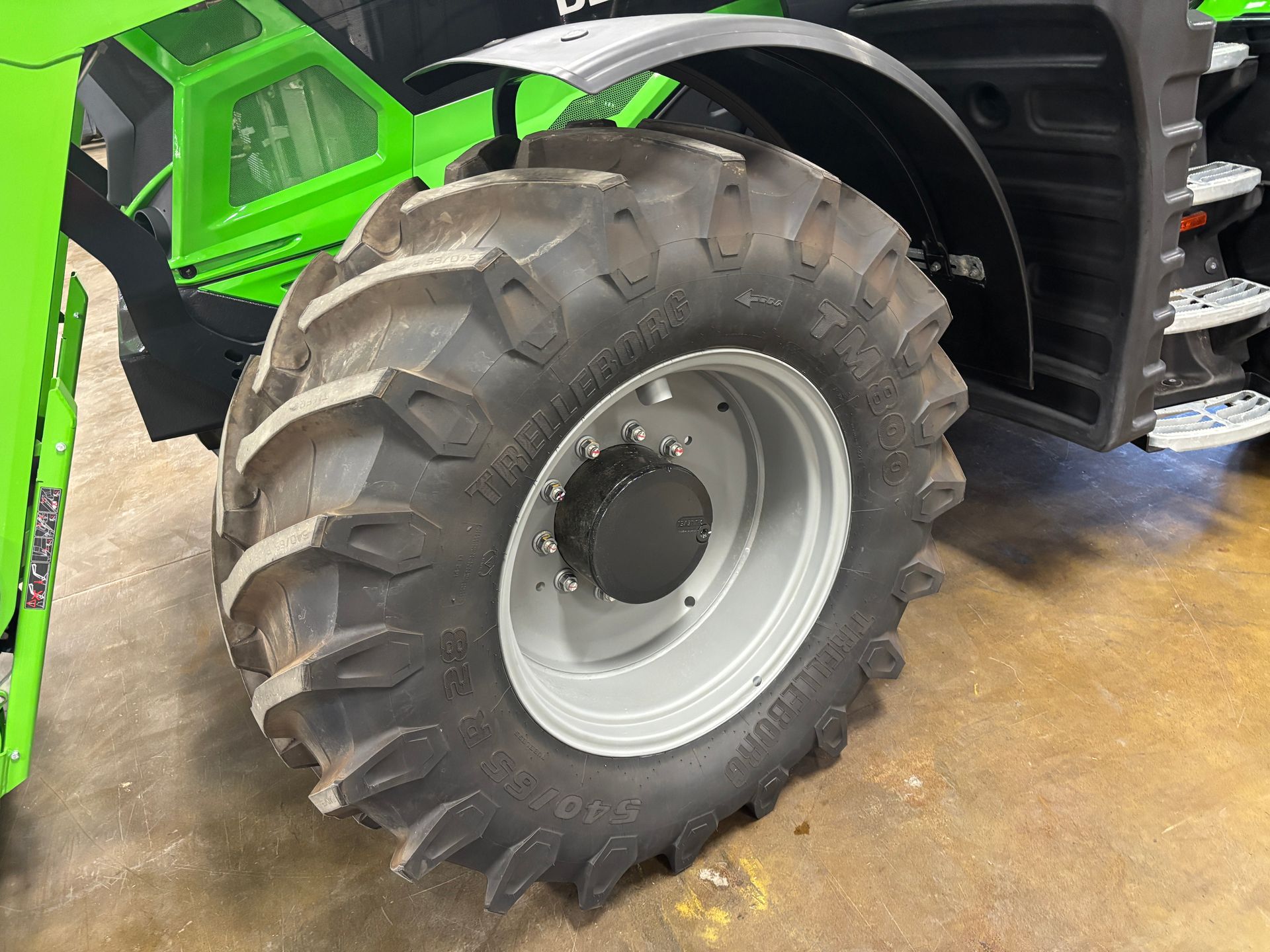 Close-up of a large tractor tire. The tire is black with deep treads, mounted on a silver wheel.